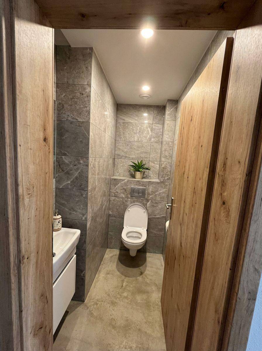 Modernes Gäste-WC mit grauen Marmorfliesen, wandhängender Toilette und kleinem Waschbecken.