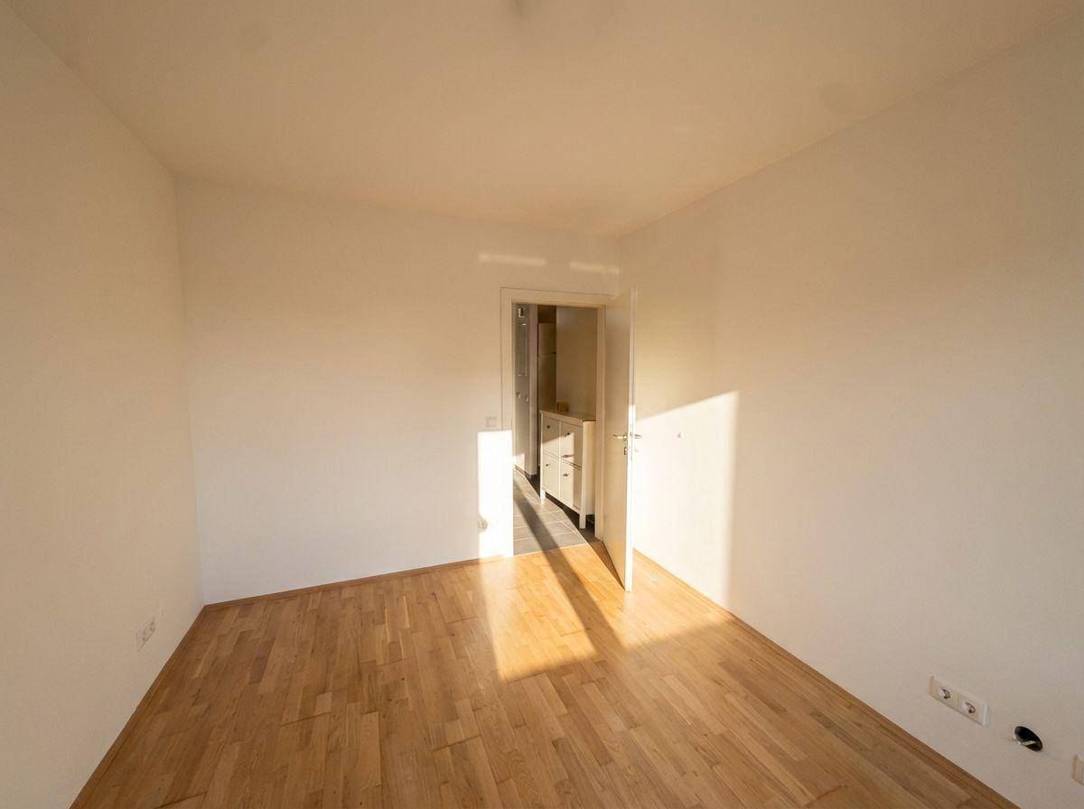 Leeres Zimmer mit Holzboden und viel Tageslicht, geeignet als Schlaf- oder Arbeitszimmer.