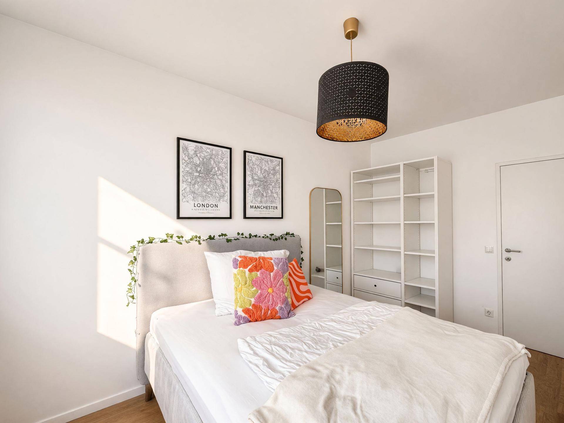 Helles Schlafzimmer mit einem bequemen Bett, einem Bücherregal und dekorativen Wandbildern.