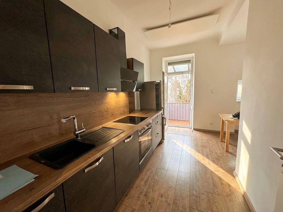 Moderne Einbauküche mit dunklen Schränken, Holzarbeitsplatten und Zugang zu einem Balkon.