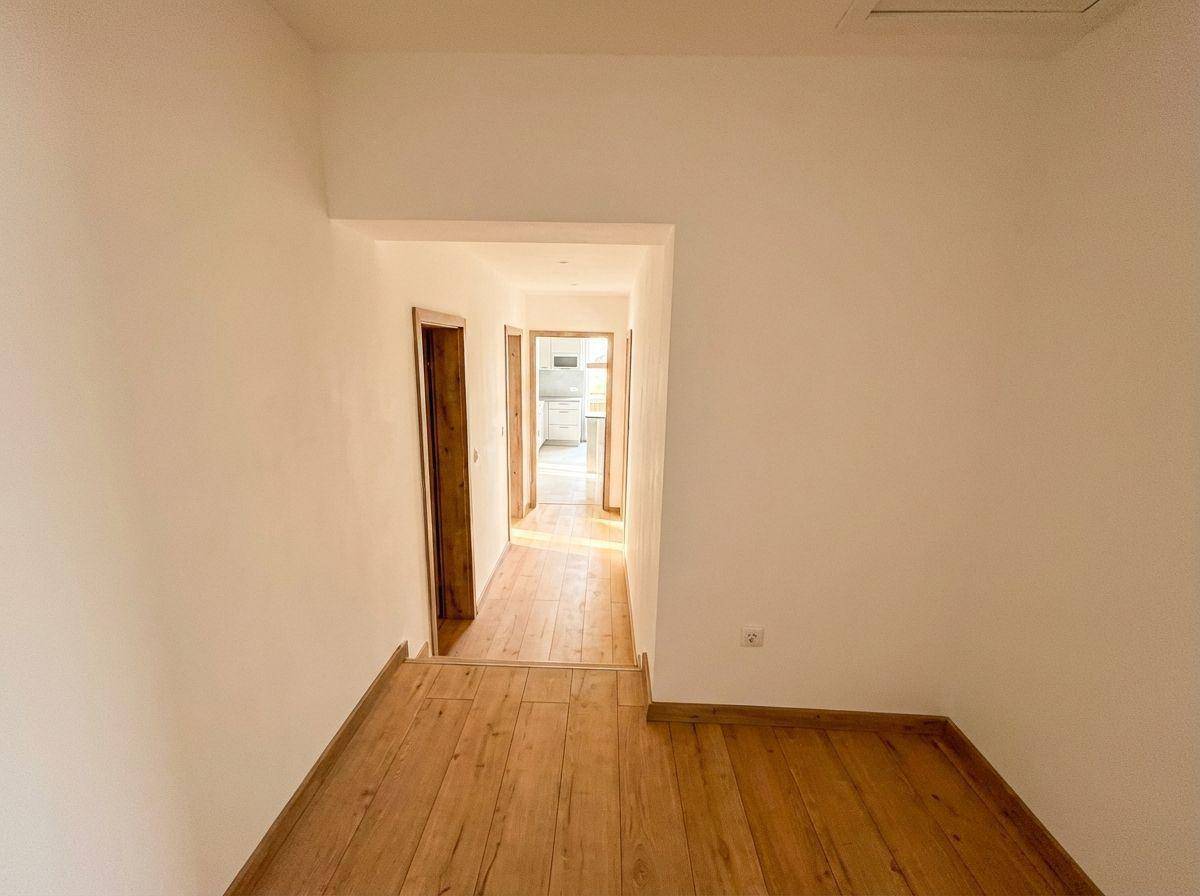 Heller Flur mit Holzboden und weißen Wänden, der zu weiteren Zimmern im Haus führt.