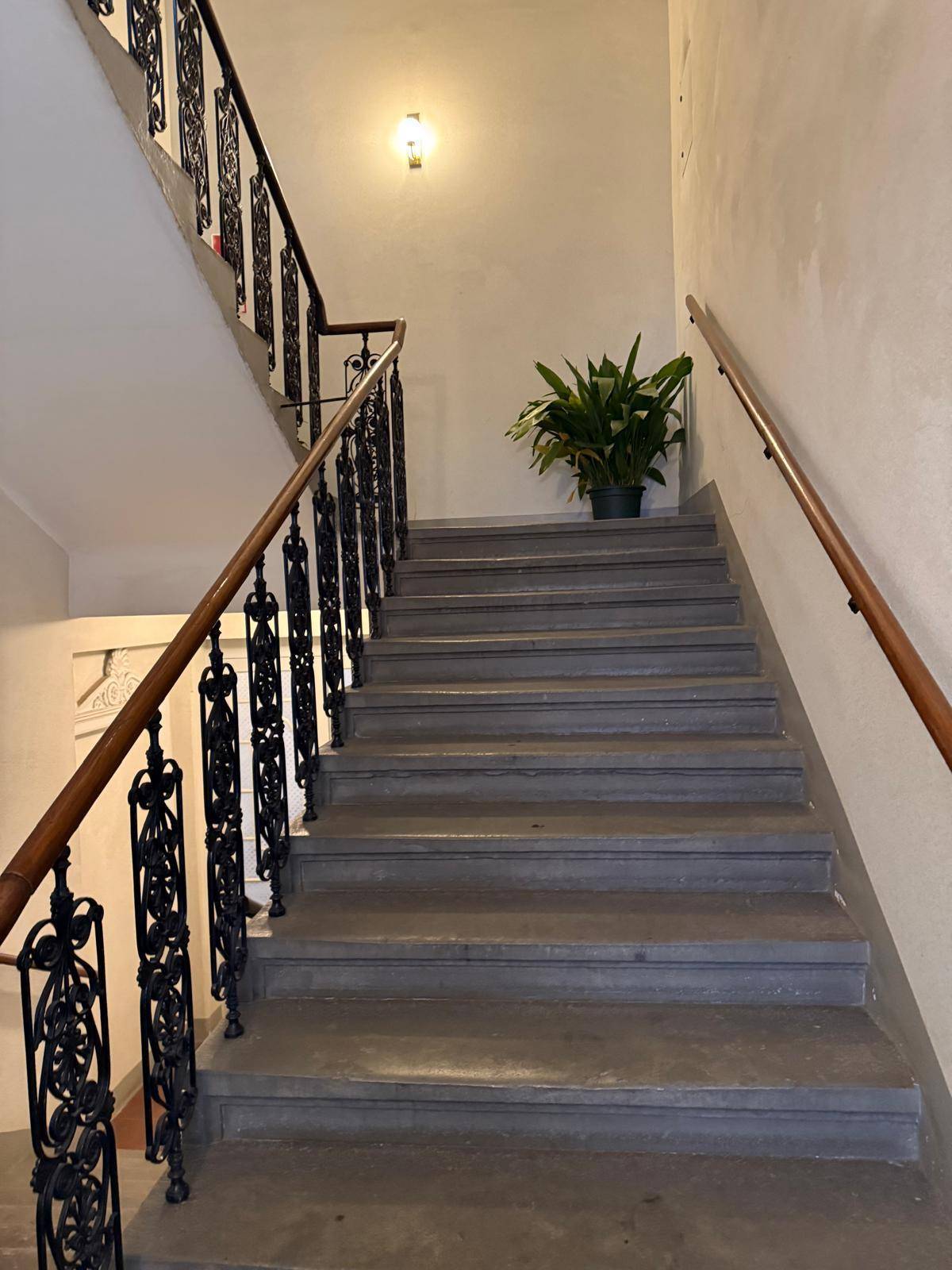 Treppenhaus mit Steinstufen, schmiedeeisernem Geländer und Holzhandlauf in einem Altbau.
