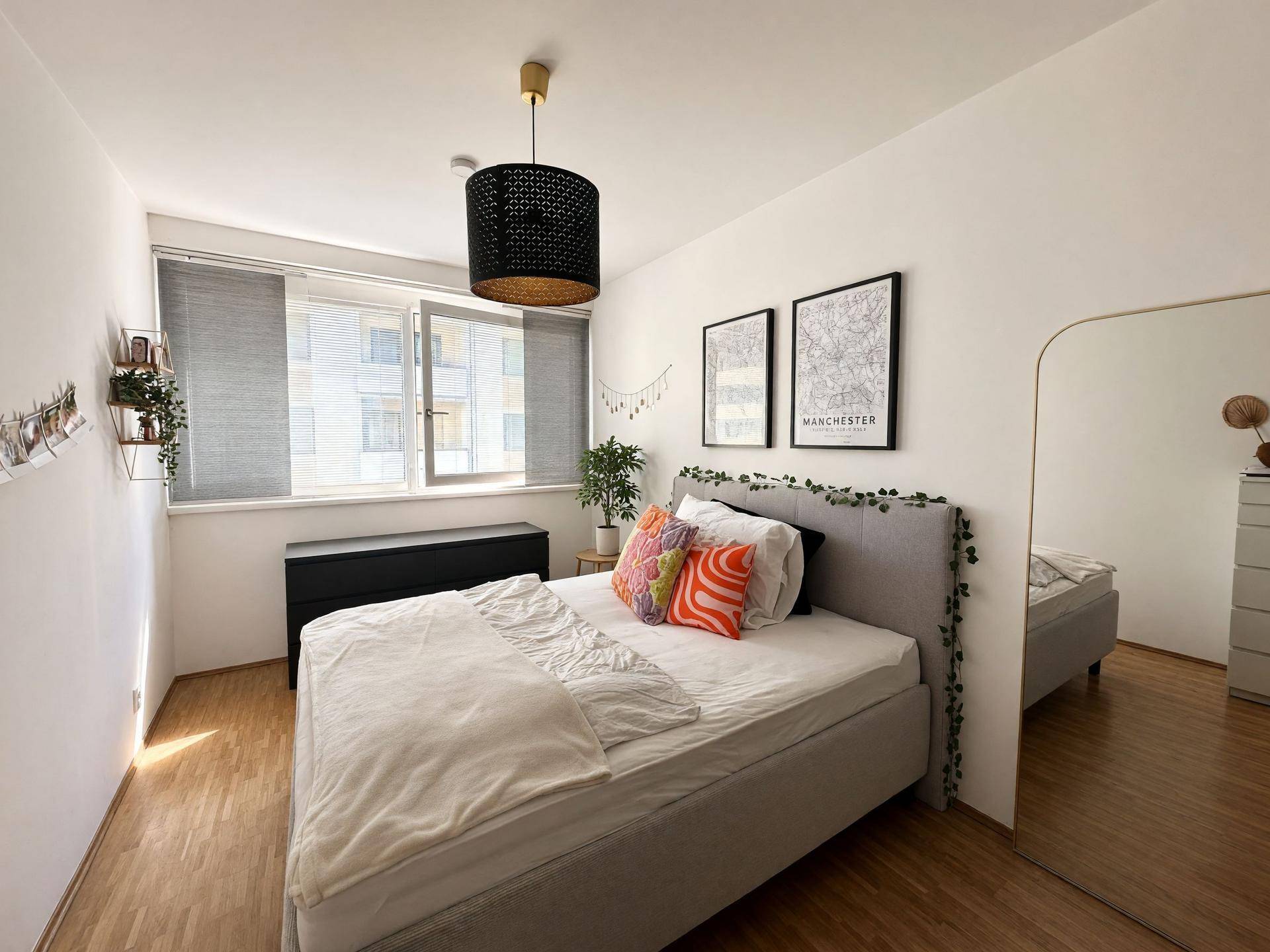 Schlafzimmer mit Fenster, das viel Tageslicht hereinlässt, und einem großen Spiegel.