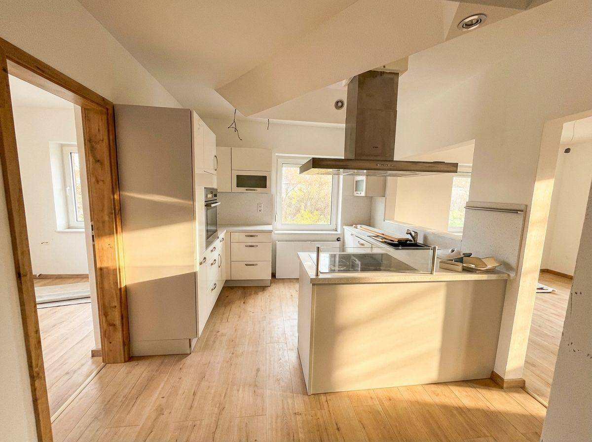 Helle, moderne Küche mit weißen Schränken, Kochinsel und Holzboden, durchflutet von Sonnenlicht.