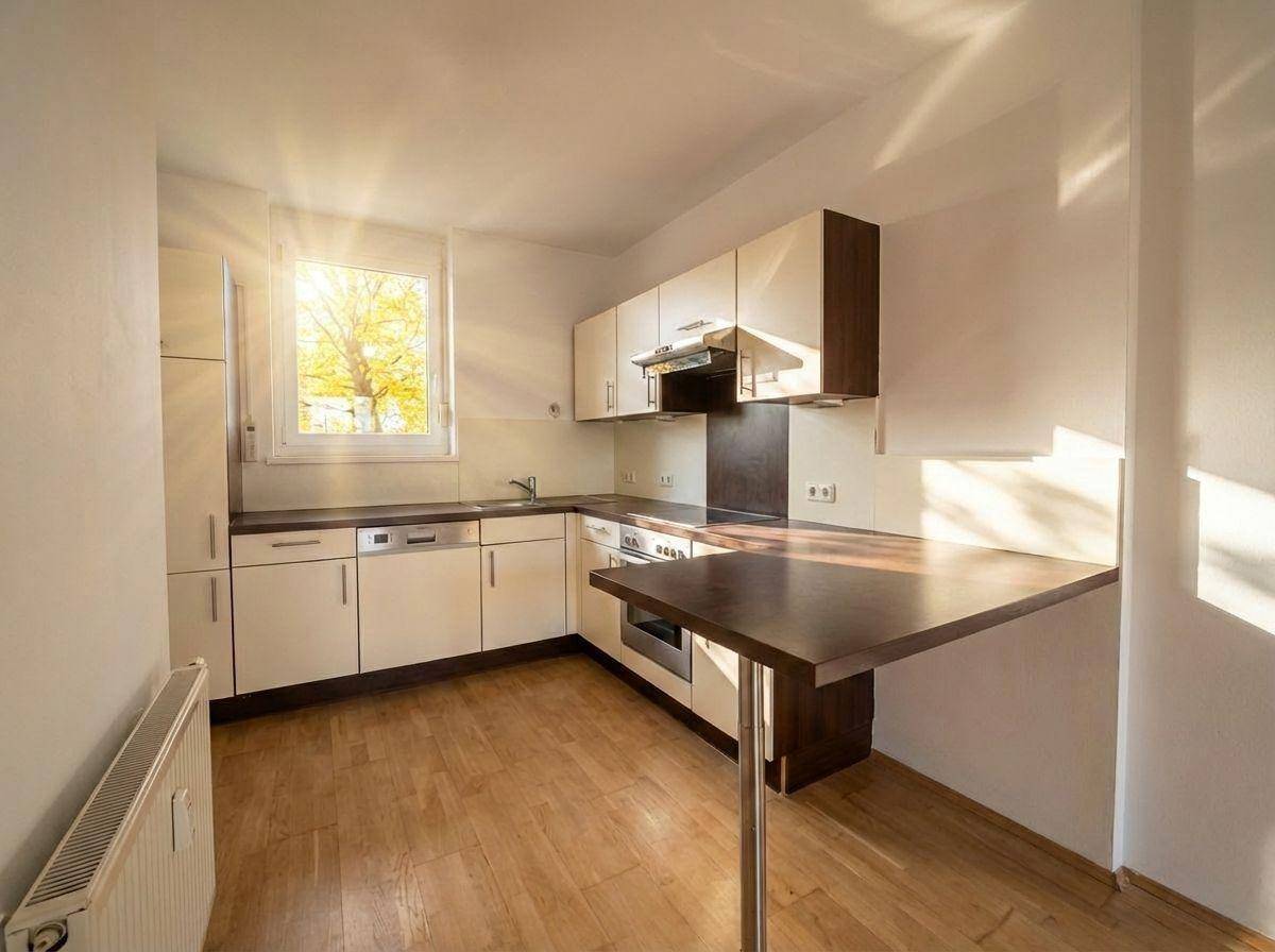 Funktionale Küche mit hellen Schränken, dunkler Arbeitsplatte und einem kleinen Frühstückstresen.