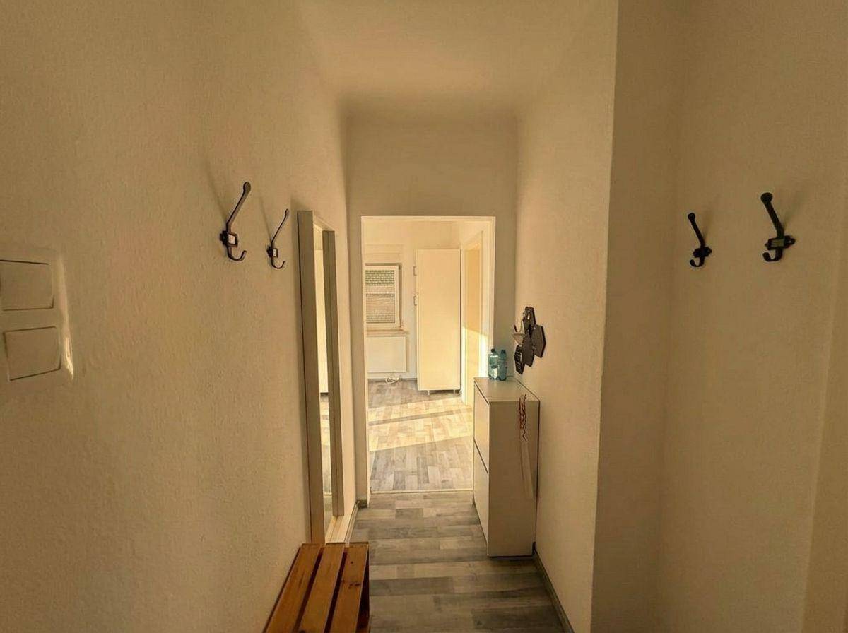 Heller Flur mit Garderobenhaken, Spiegel und Schuhschrank, der zu weiteren Räumen führt.