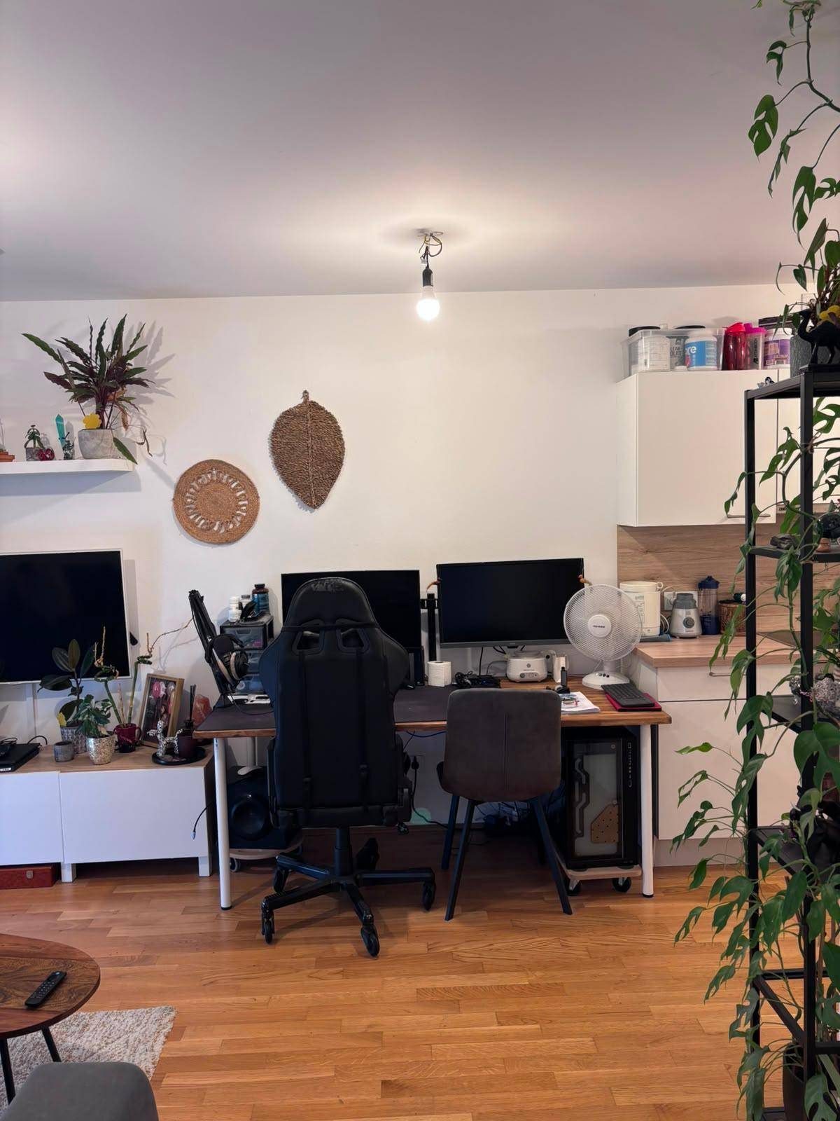 Wohnbereich mit Schreibtisch, zwei Monitoren und Holzboden.