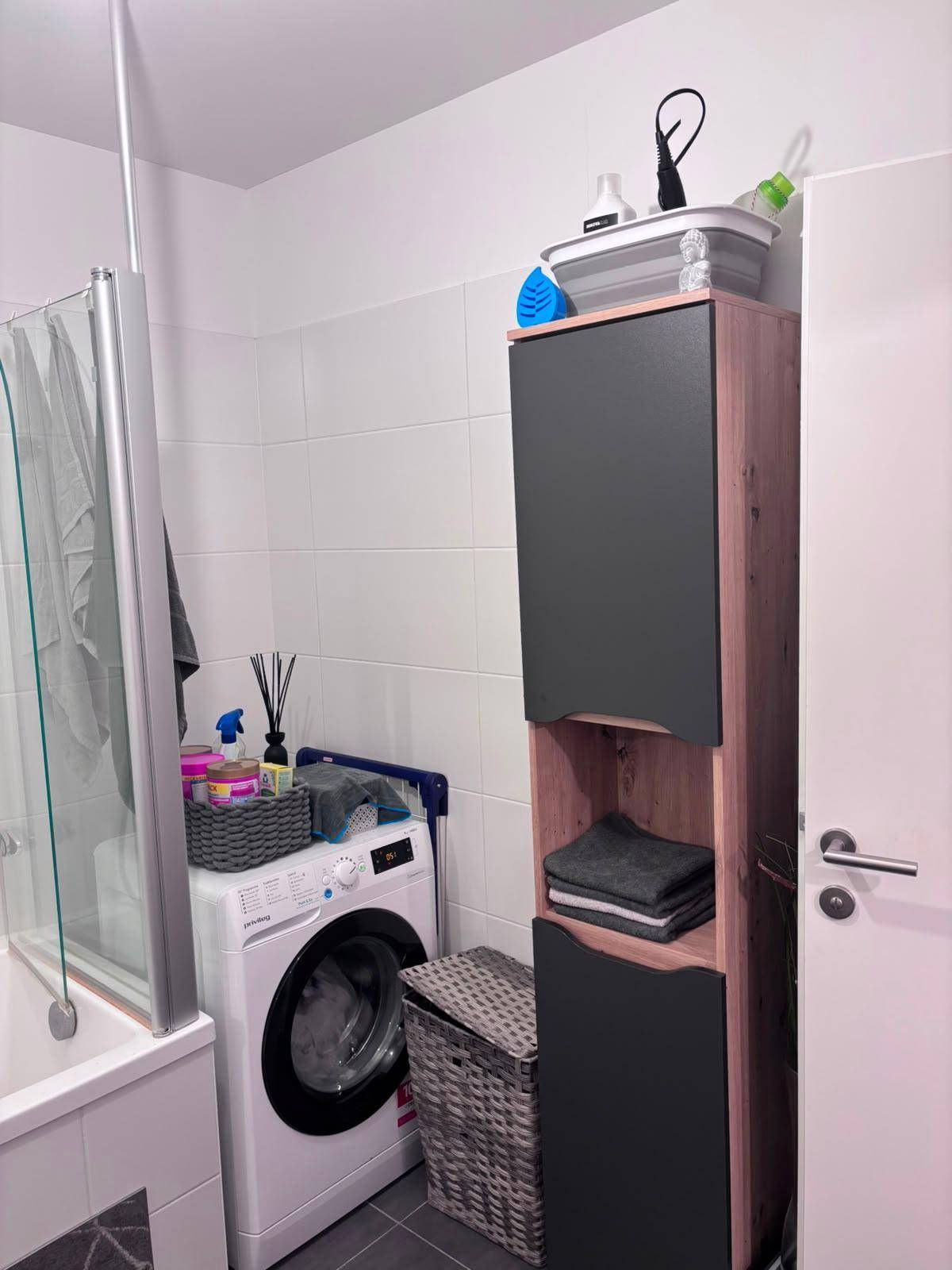 Badezimmer mit Waschmaschine, Badewanne und praktischem Hochschrank.