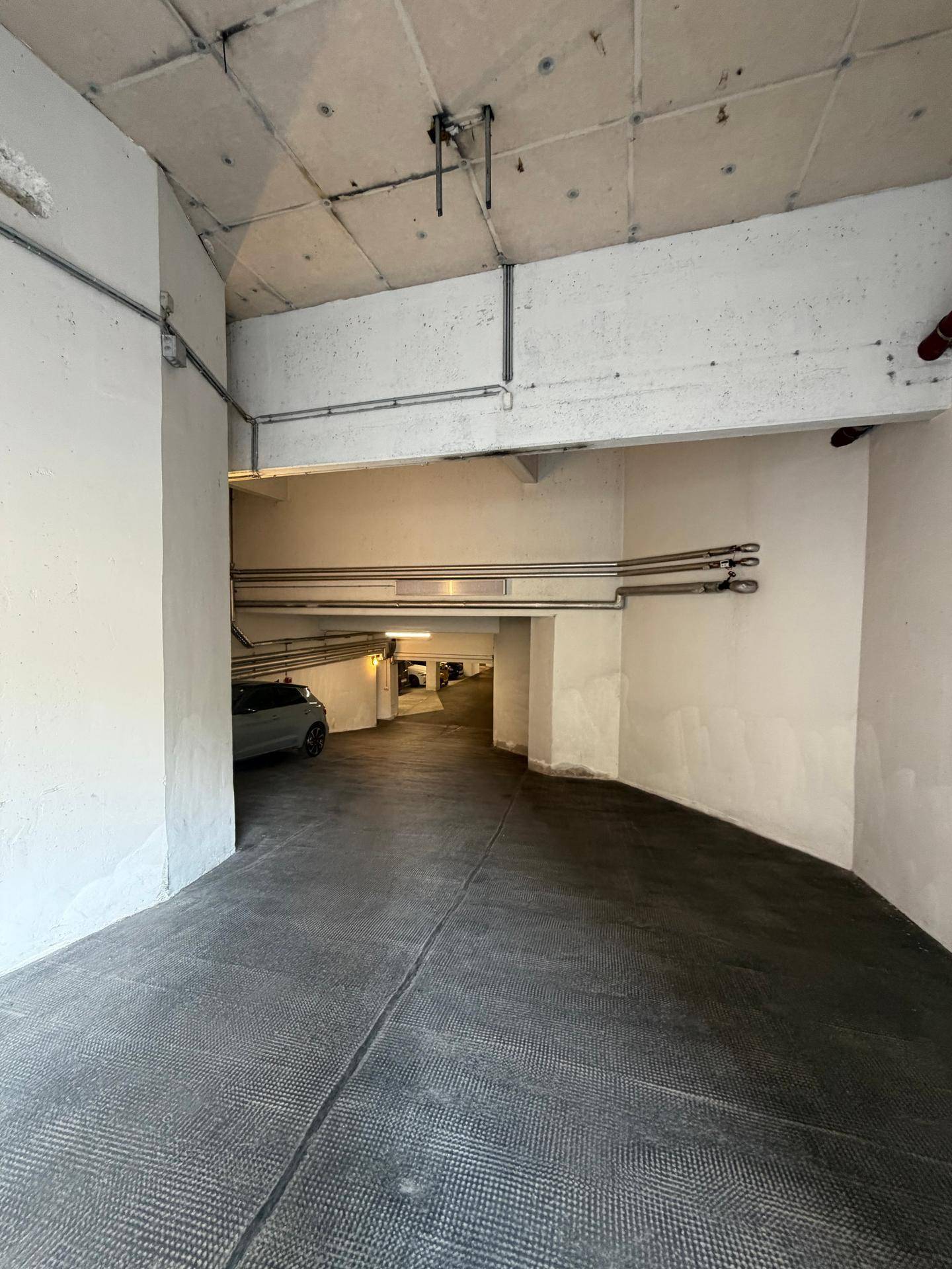 Eine geschwungene Rampe führt in eine helle Tiefgarage mit einem geparkten Fahrzeug im Hintergrund.