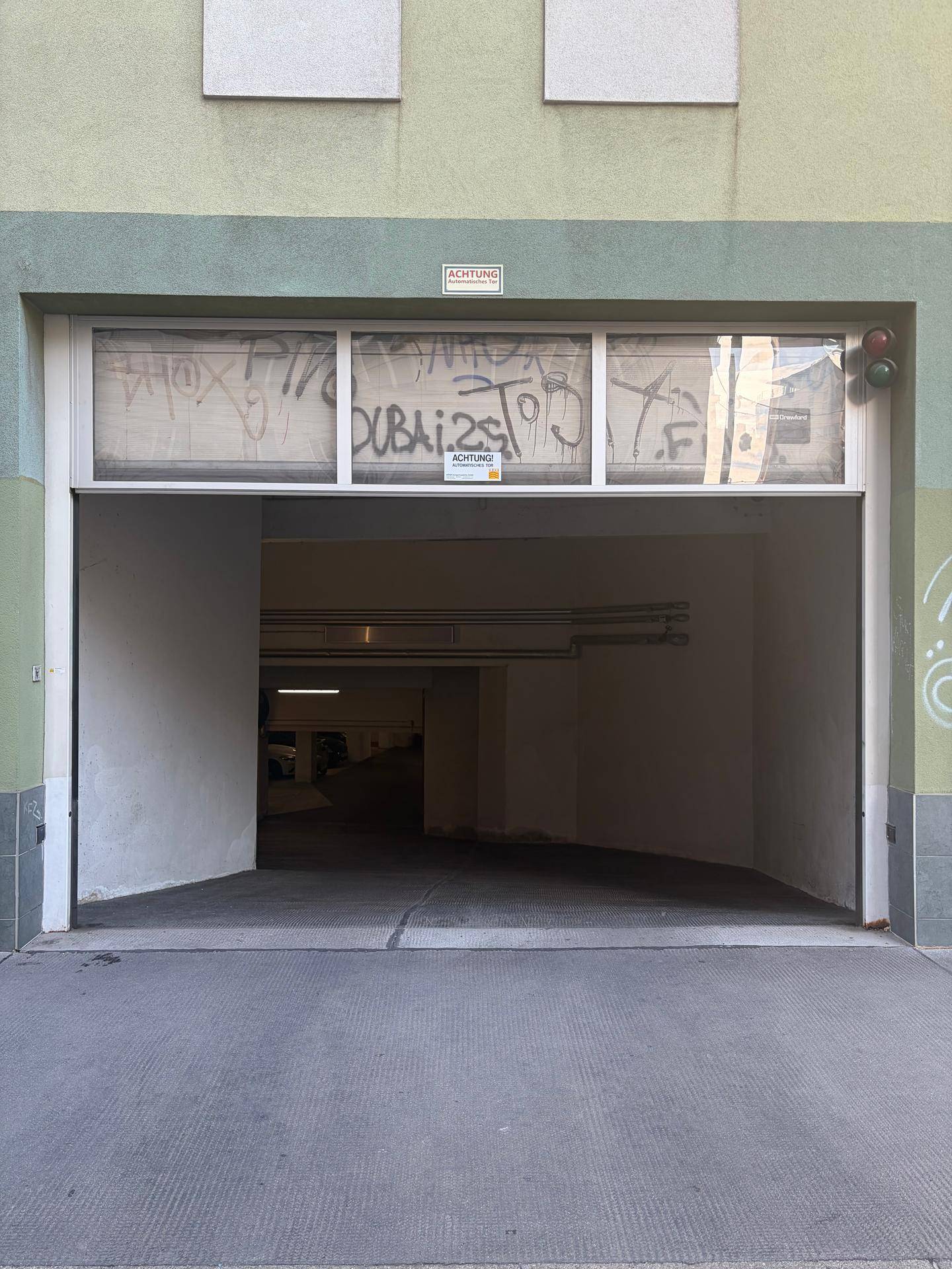 Offene Garageneinfahrt eines Gebäudes, die zu einer Tiefgarage mit Rampe führt.