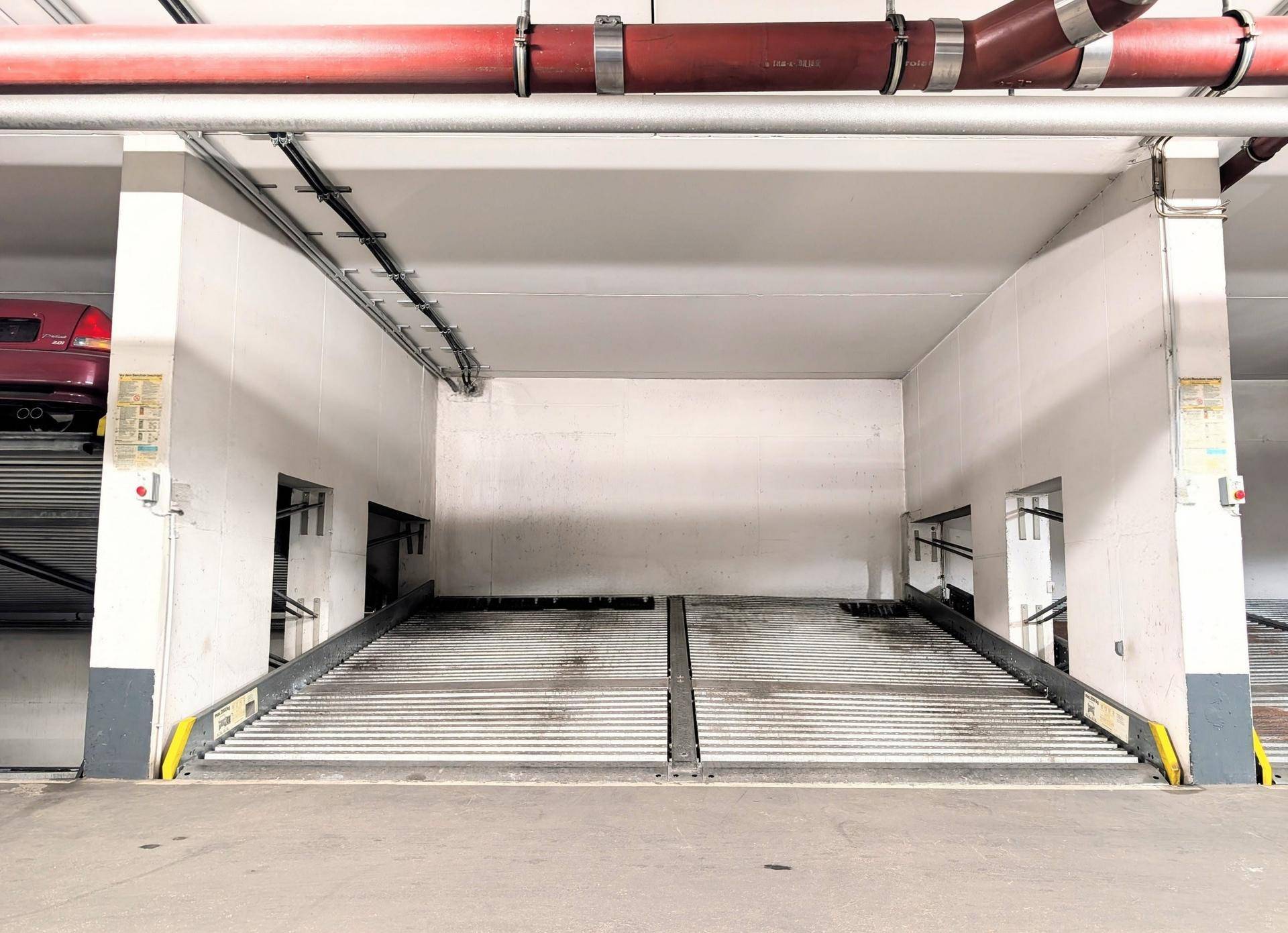 Tiefgarage mit mechanischen Parksystemen für Fahrzeuge und sichtbaren Rohrleitungen.