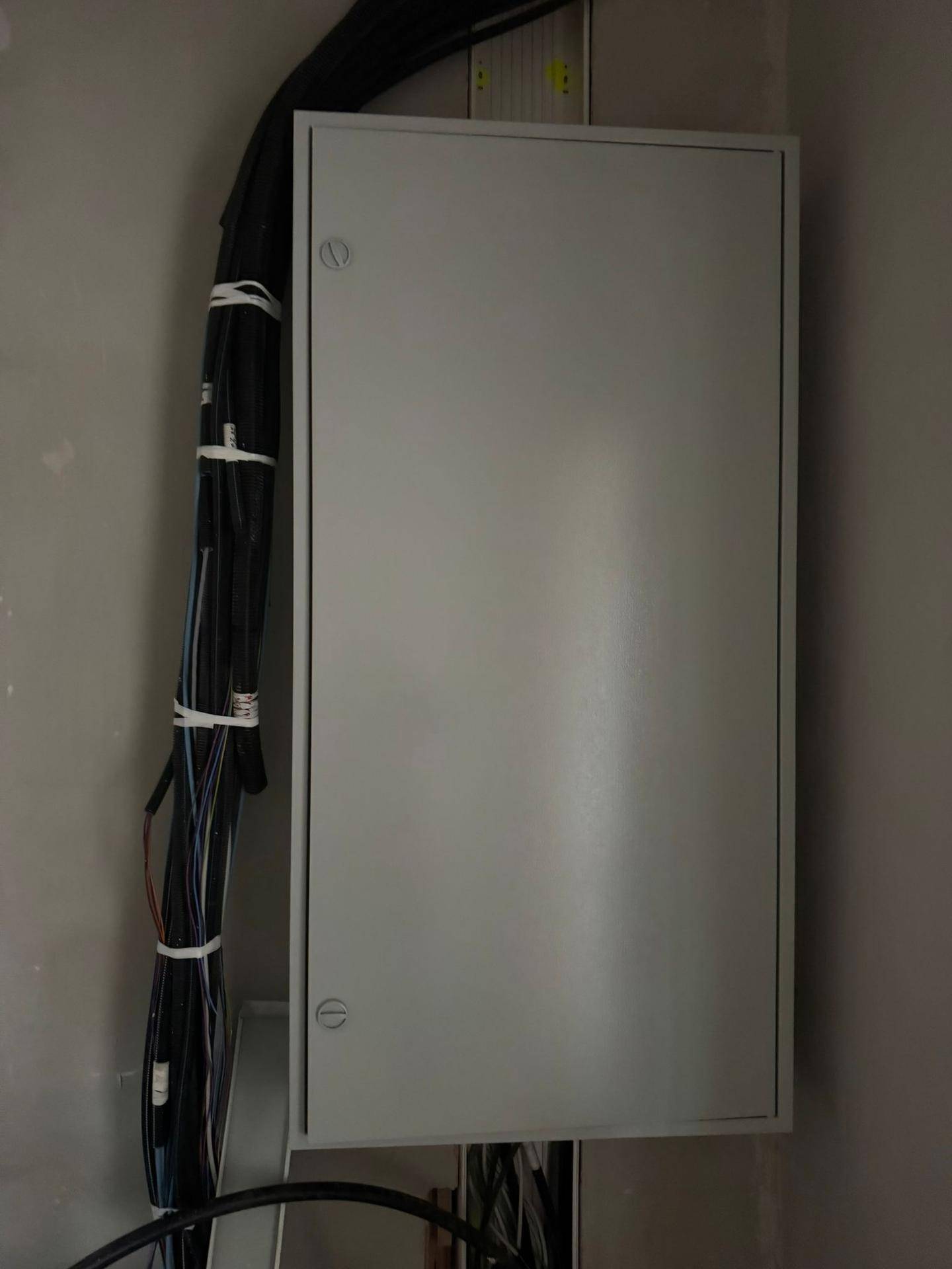 Geschlossener elektrischer Verteilerkasten an der Wand in einem Raum im Rohbau.