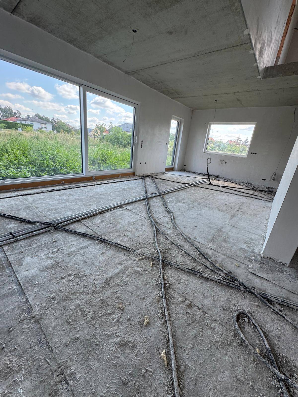 Großer Innenraum im Rohbau mit vielen Leitungen auf dem Boden und weitem Blick durch die Fenster.