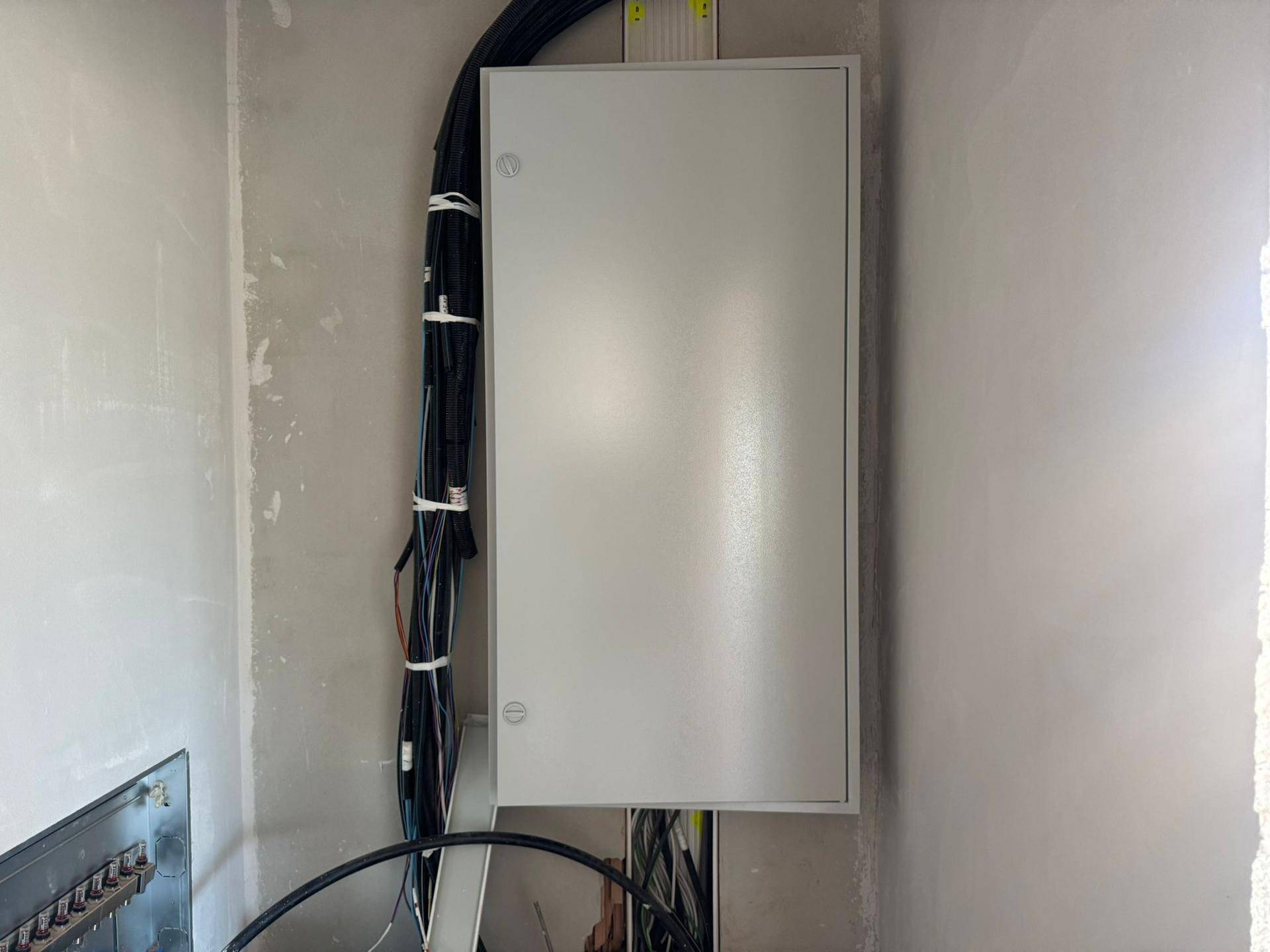 Elektrischer Verteilerkasten an der Wand in einem Raum im Rohbau mit vielen Kabeln.