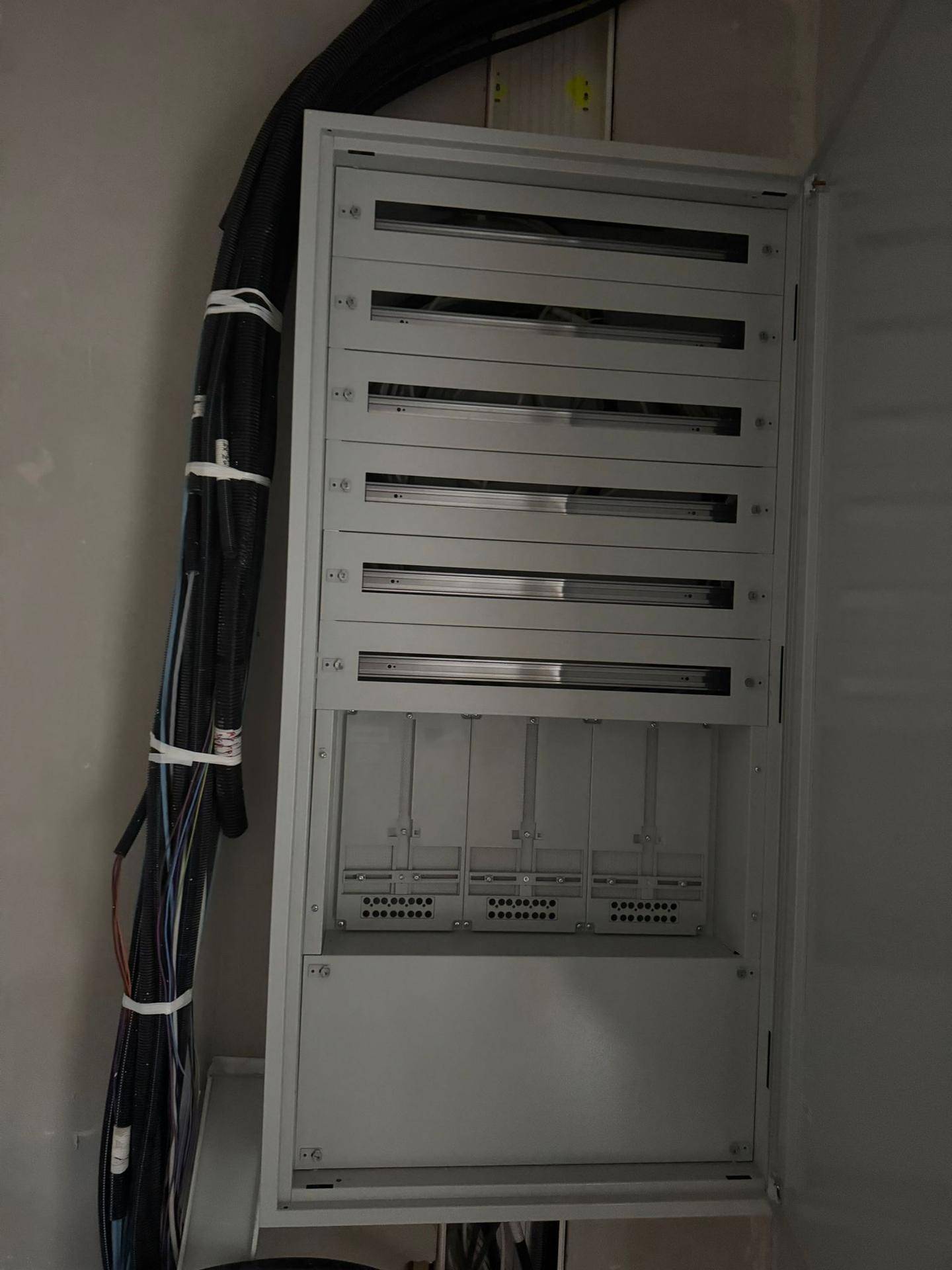 Offener elektrischer Verteilerkasten mit Sicherungen und Verkabelung in einem Rohbauraum.