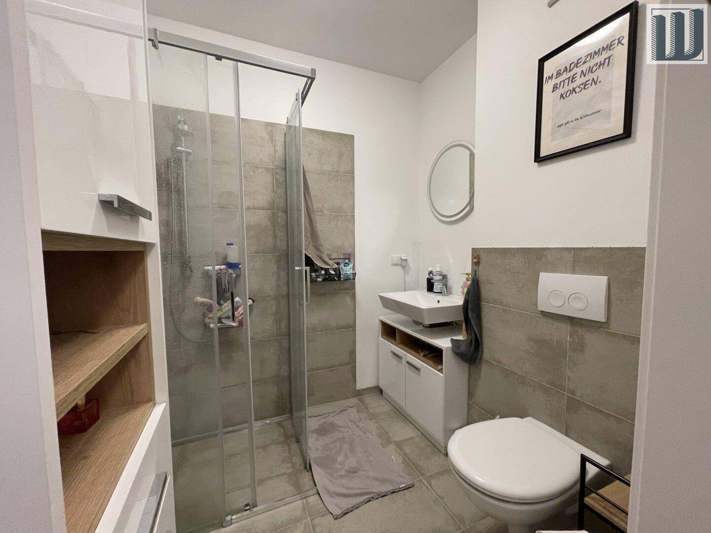 Modernes Badezimmer mit Duschkabine, Wand-WC und Waschbecken, in hellen Grautönen gefliest.