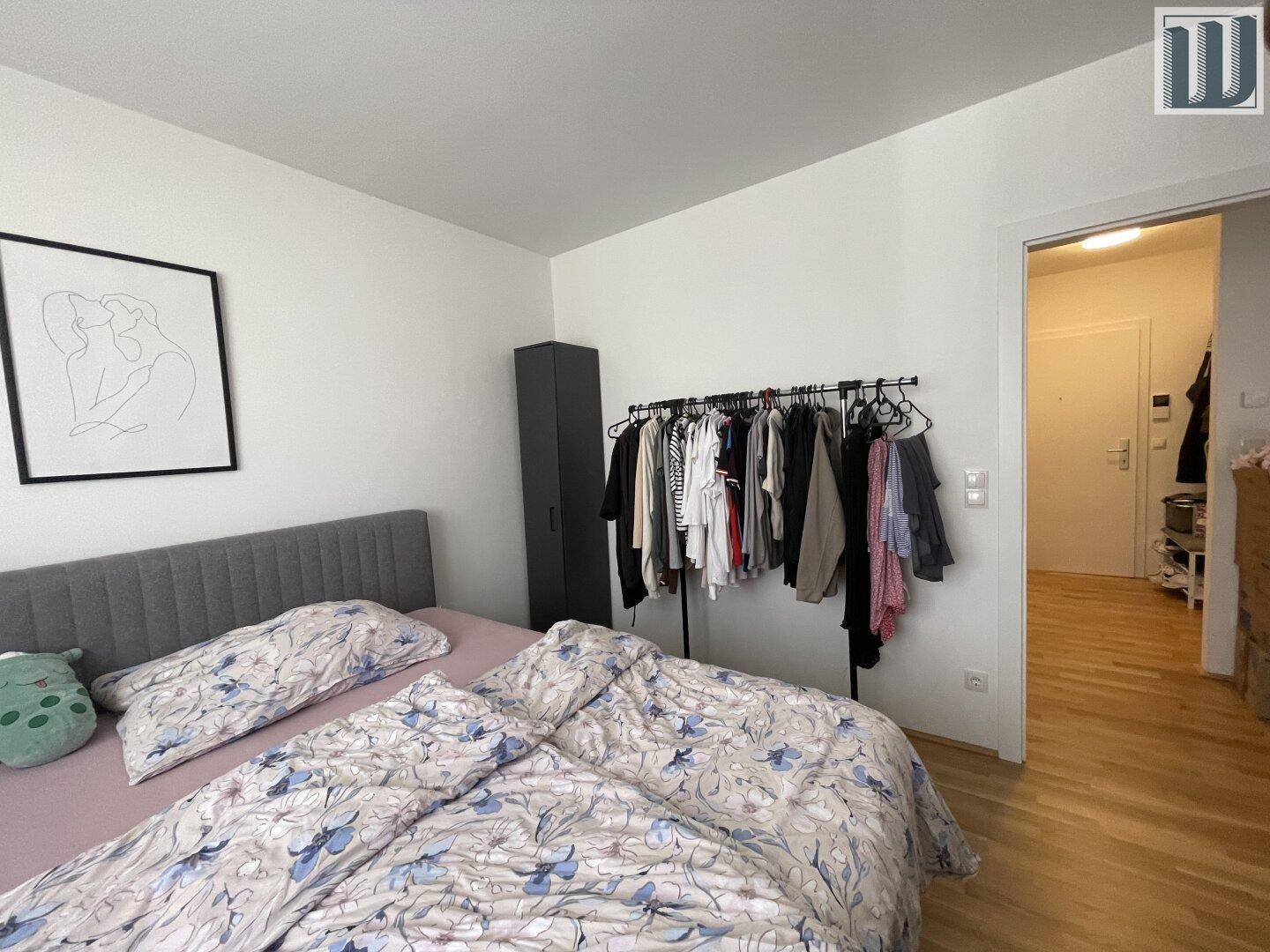Schlafzimmer mit Doppelbett und Kleiderstange, Zugang zum Flur, hell und funktional.