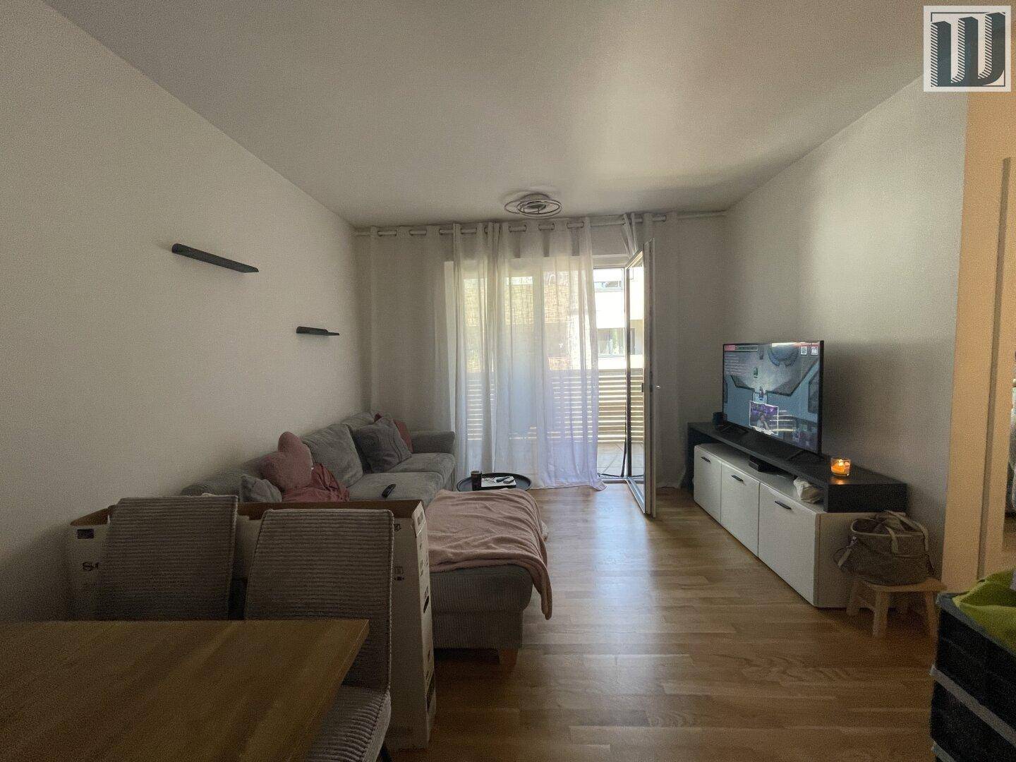 Offener Wohn- und Essbereich mit Sofa, Fernseher und Zugang zum Balkon, heller Holzboden.