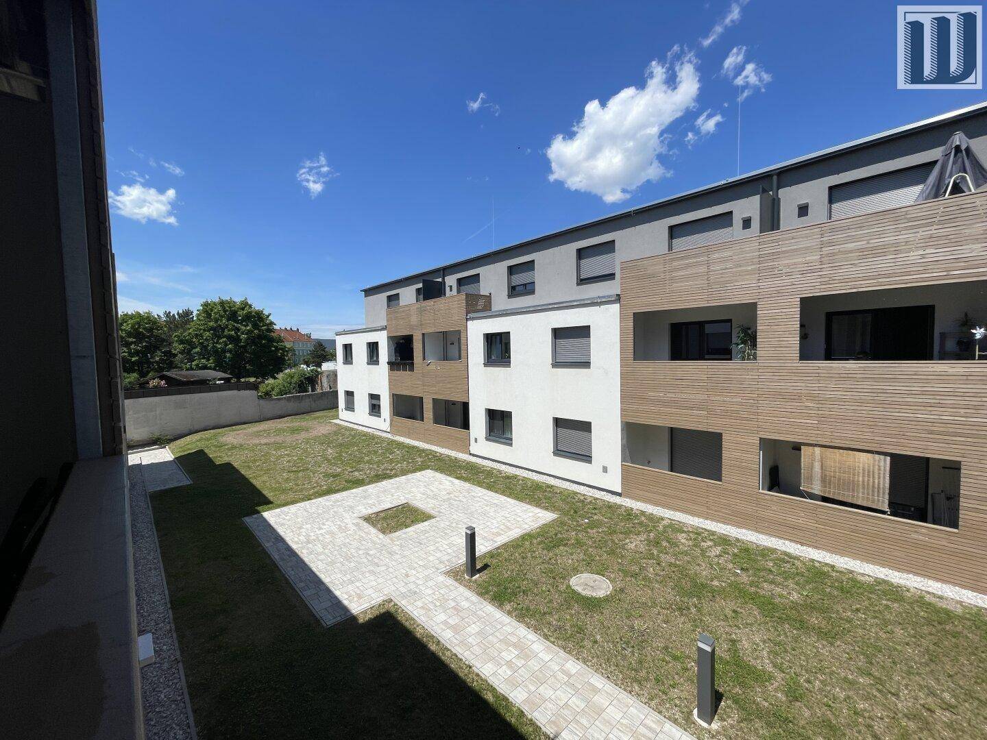 Geräumiger Balkon mit Blick auf den gepflegten Innenhof und die moderne Fassade des Gebäudes.