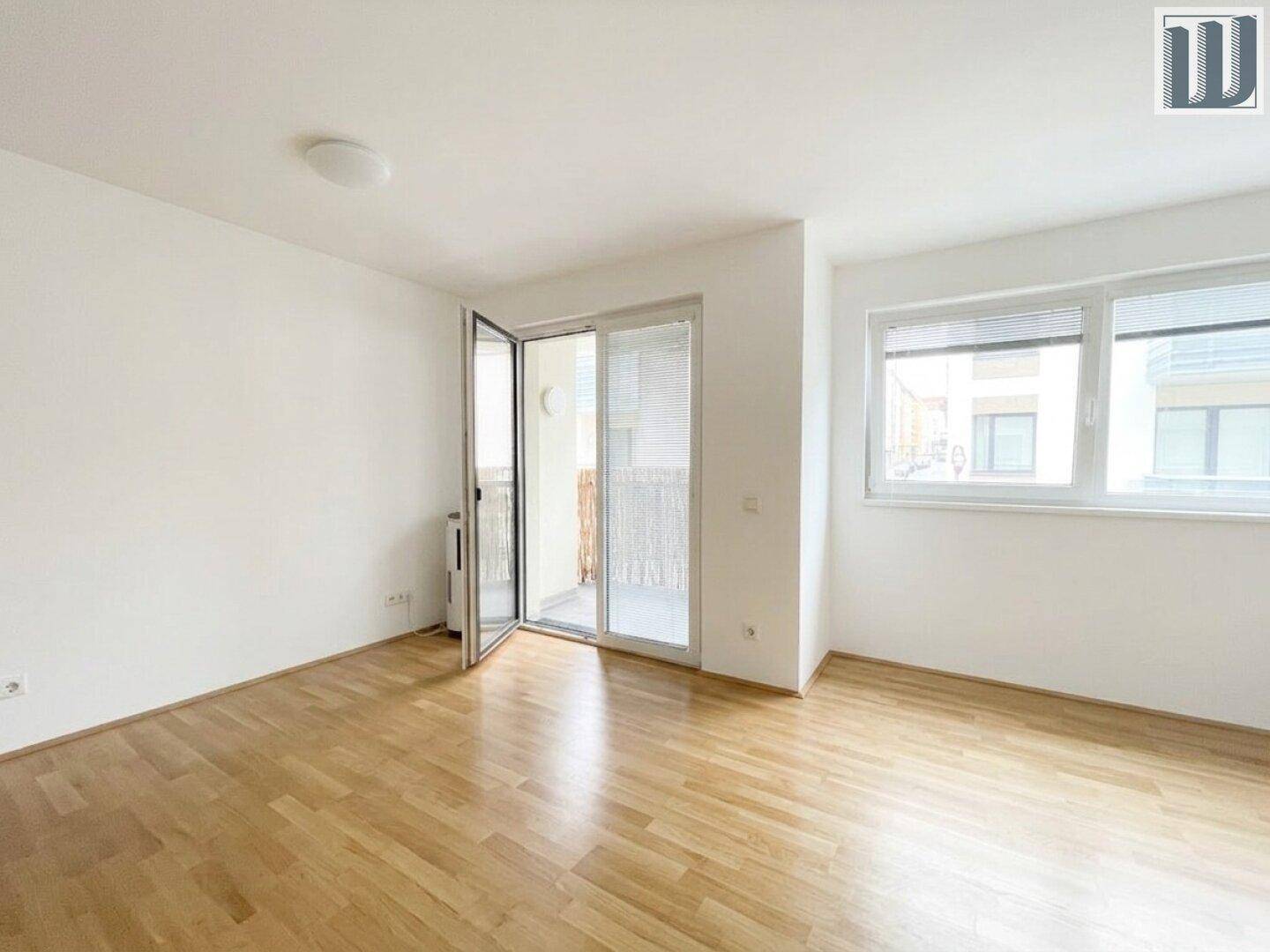 Heller Wohnraum mit Parkettboden und Zugang zu einem Balkon, ausgestattet mit großen Fenstern.
