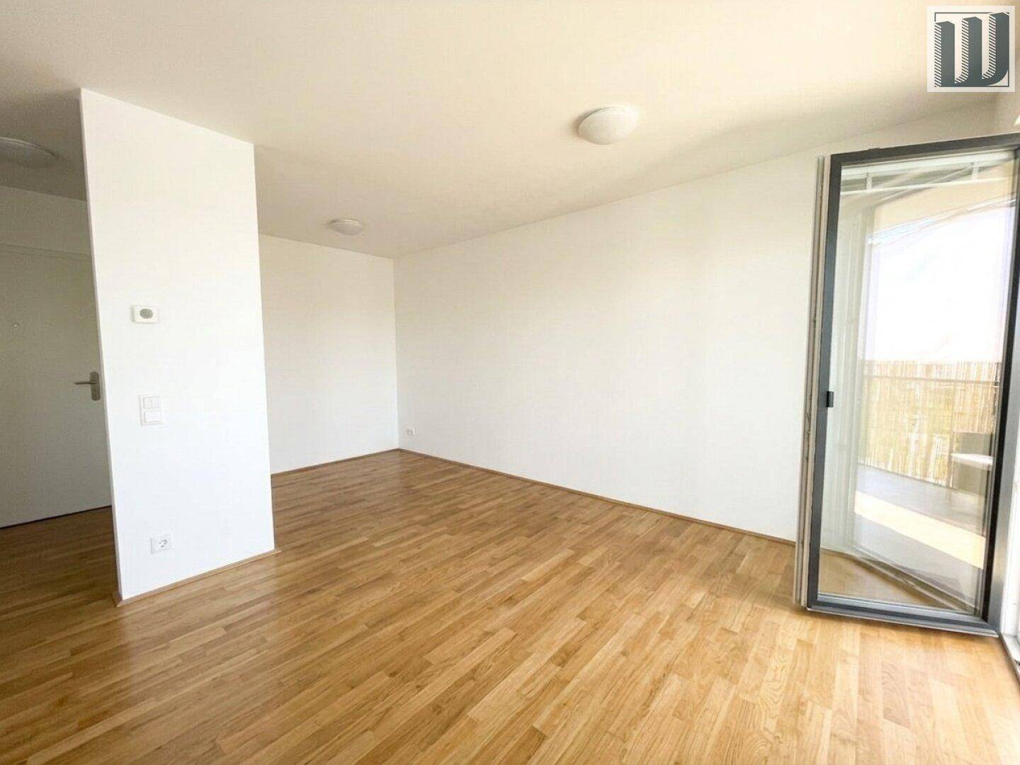 Geräumiger Wohnbereich mit Parkettboden und großem Fenster mit Zugang zum Balkon.