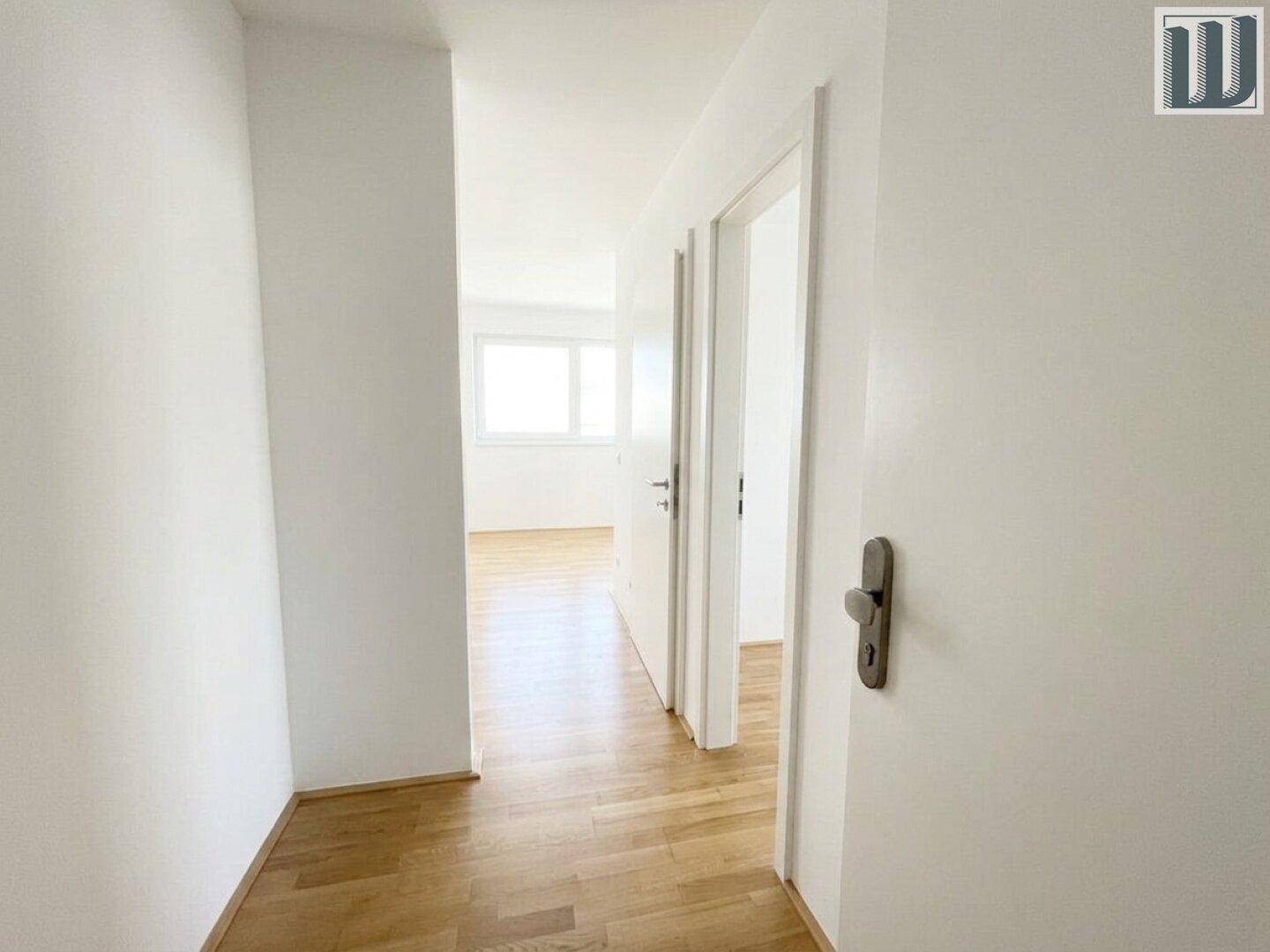 Heller Flur mit Parkettboden und weißen Wänden, der zu weiteren Räumen führt.