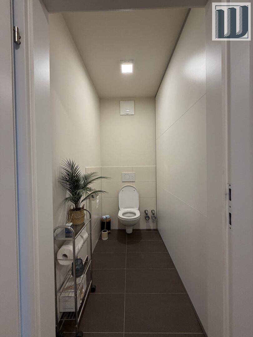 Separates WC mit Wand-WC und Fliesenboden, ausgestattet mit einem kleinen Regal.