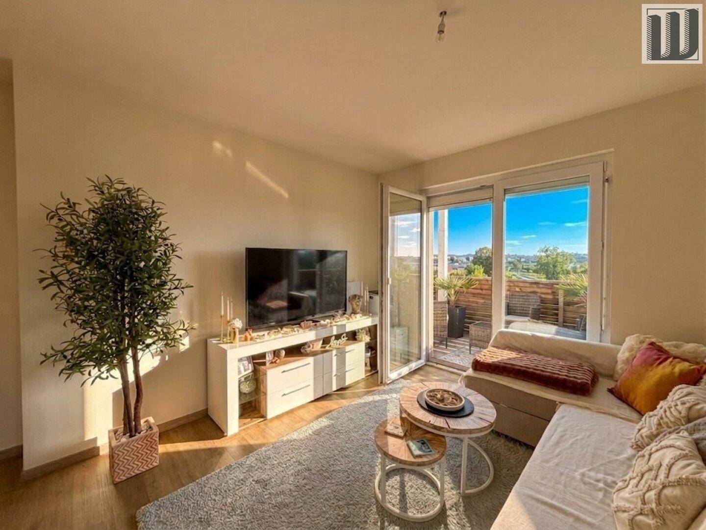 Gemütliches Wohnzimmer mit Sofa, Fernseher und Zugang zu einem sonnigen Balkon.