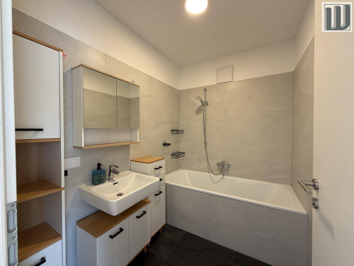 Modernes Badezimmer mit Badewanne, Waschbecken und Spiegelschrank in hellen Grautönen.