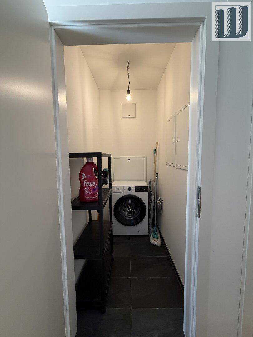 Praktischer Hauswirtschaftsraum mit Waschmaschine, Regal und dunklem Fliesenboden.