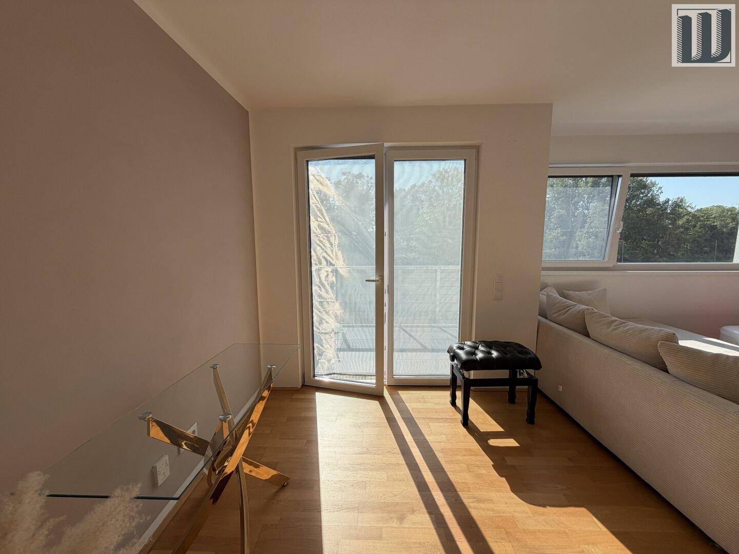 Heller Wohnraum mit Holzboden, Glastisch und Zugang zu einem sonnigen Balkon.