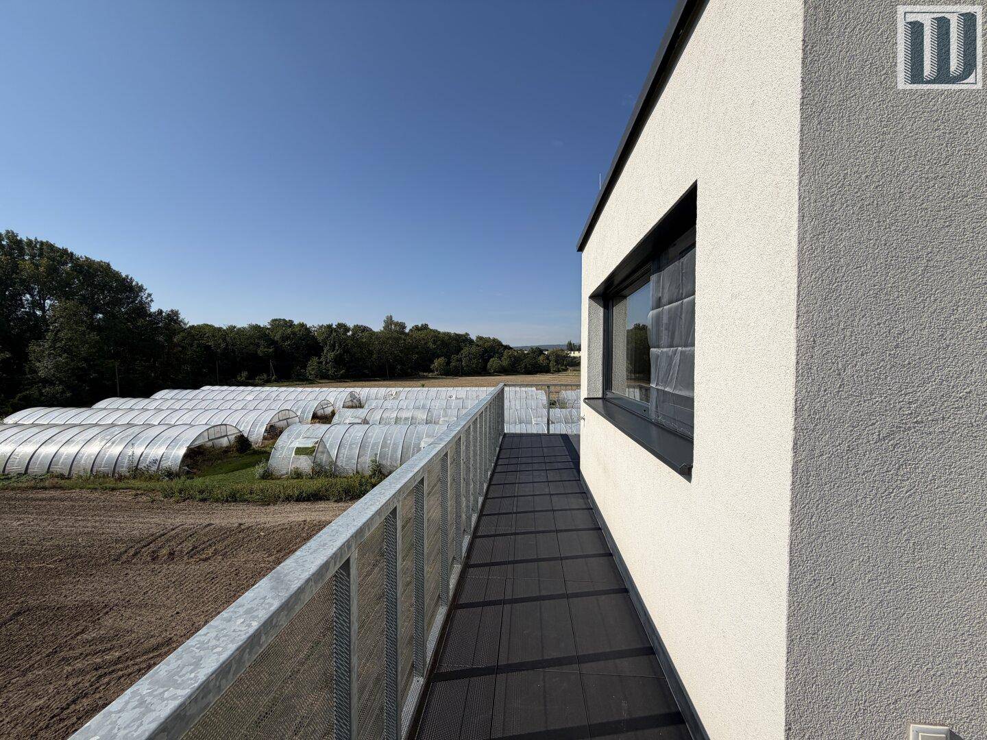 Langer Balkon mit Metallgeländer und weitem Blick über landwirtschaftliche Flächen.