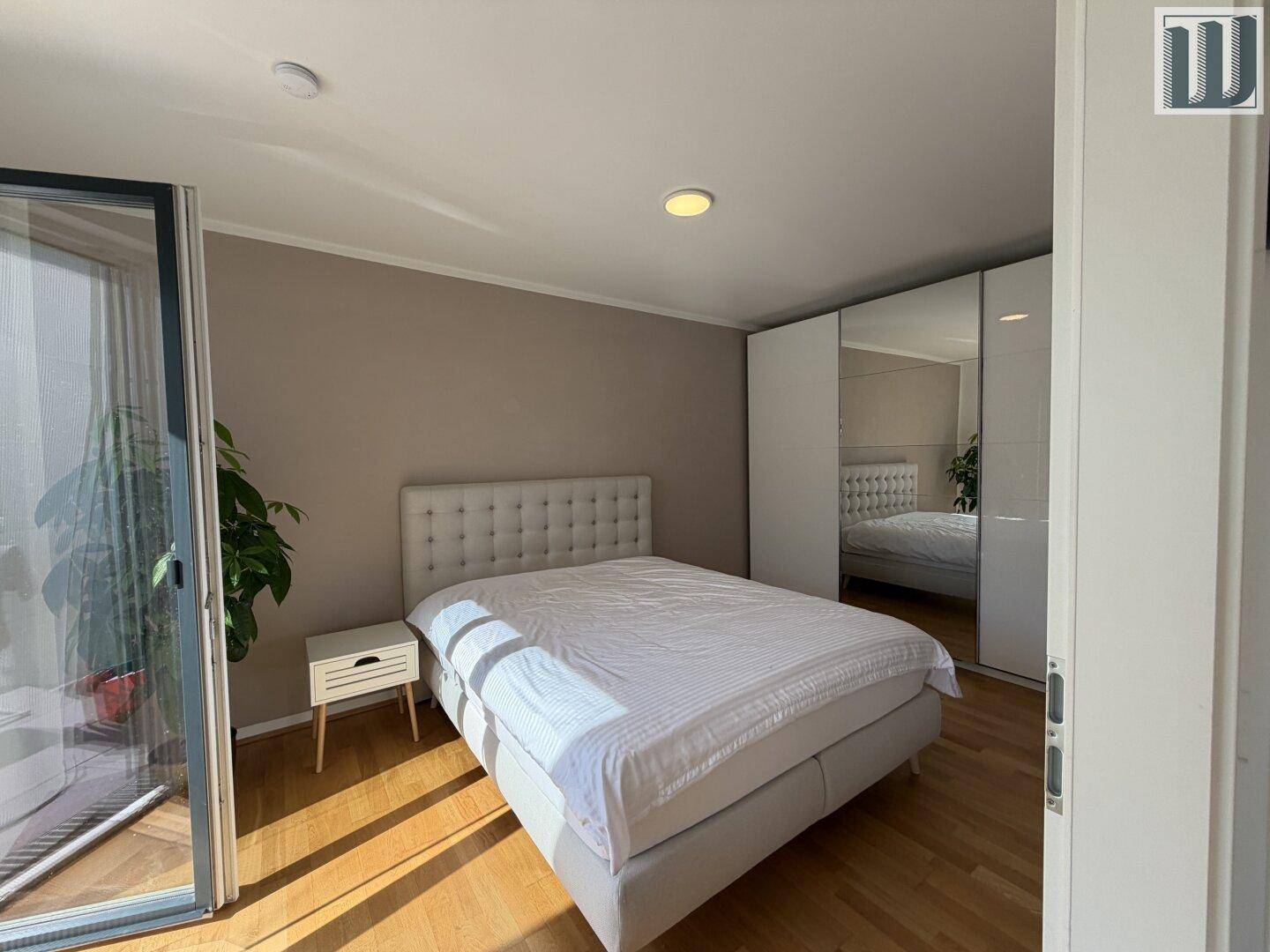 Helles Schlafzimmer mit Doppelbett, Holzboden und Zugang zu einem Balkon.