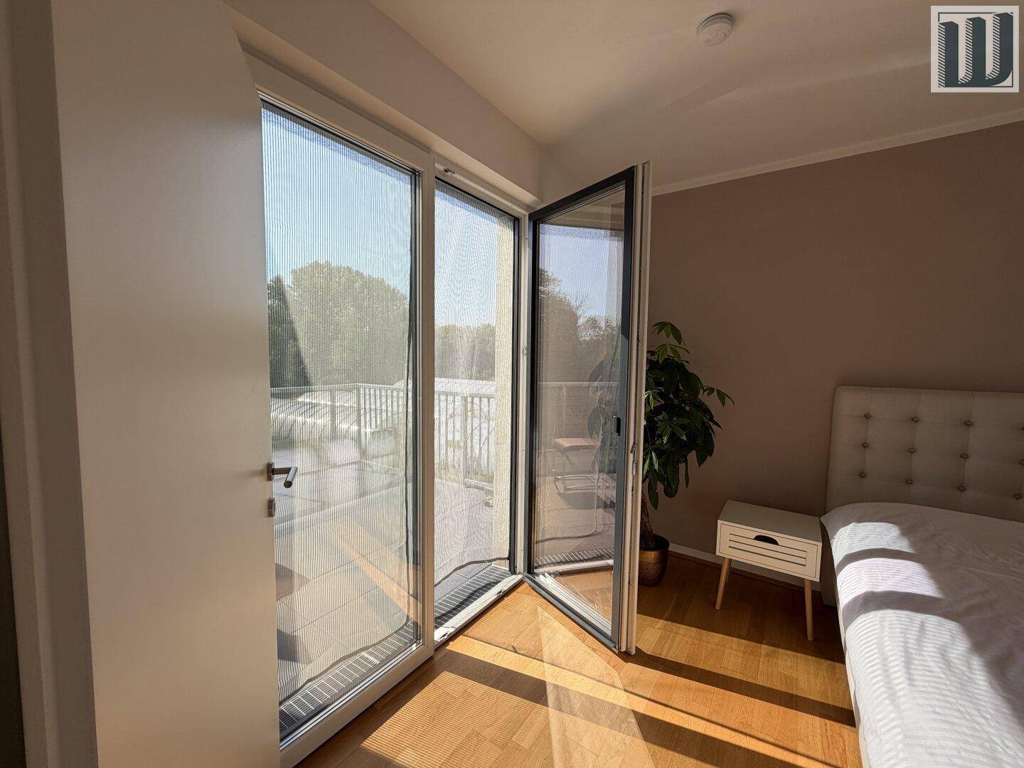 Schlafzimmer mit geöffneter Balkontür, Holzboden und viel natürlichem Licht.
