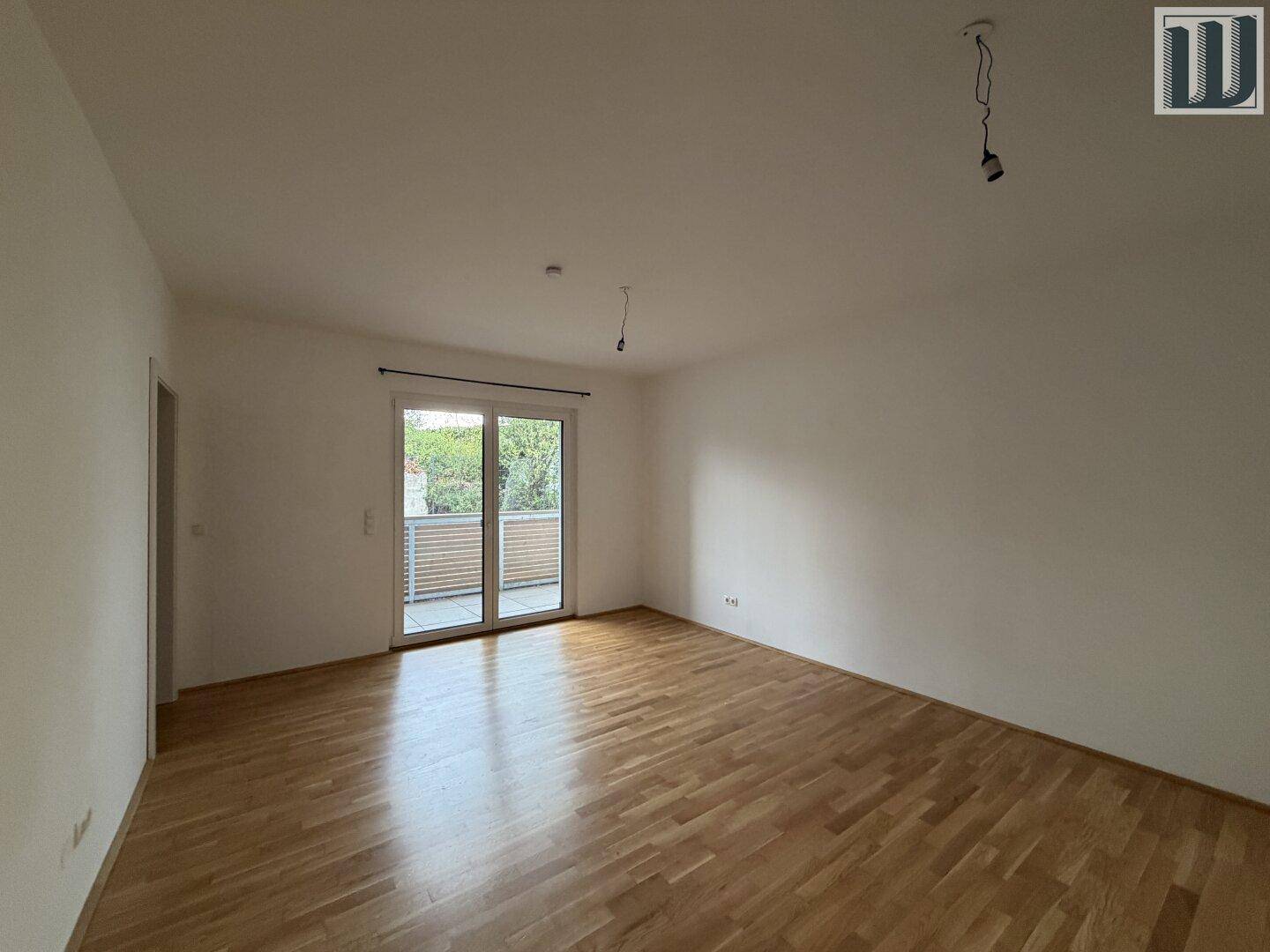 Geräumiges Wohnzimmer mit Parkettboden und großer Balkontür, die viel Tageslicht hereinlässt.