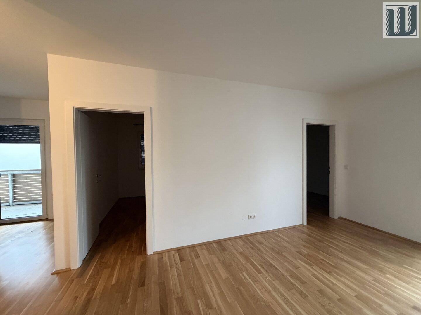 Heller Wohnbereich mit Parkettboden und Zugang zu weiteren Zimmern sowie einem Balkon.