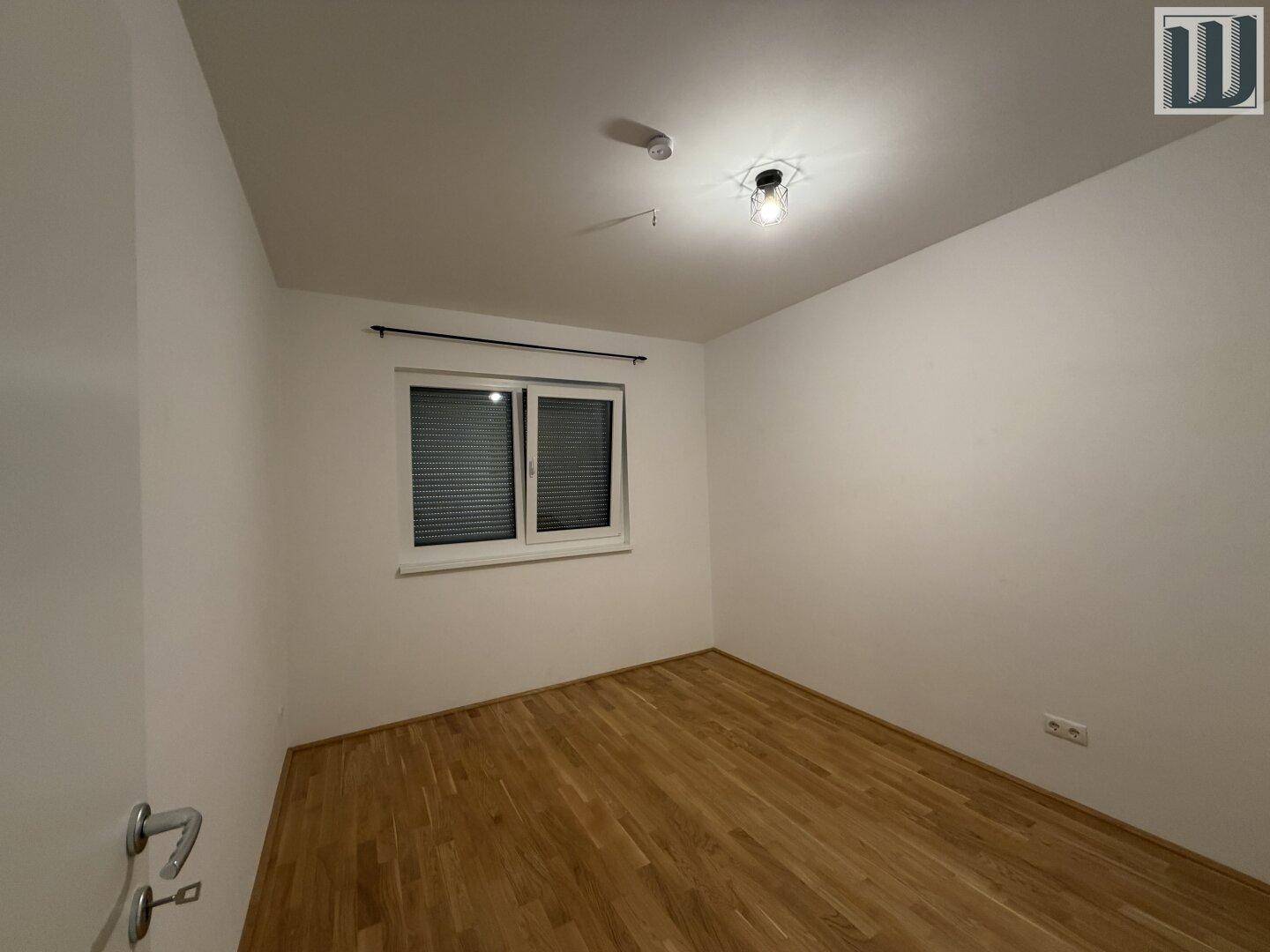 Schlafzimmer mit Parkettboden und einem Fenster mit Jalousien, bereit zur individuellen Gestaltung.
