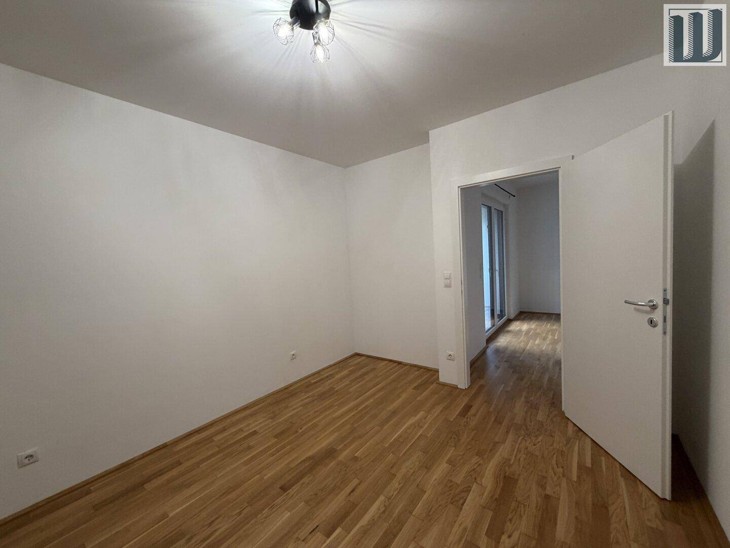Geräumiges Schlafzimmer mit Parkettboden und offener Tür, die den Blick in einen weiteren Raum freigibt.