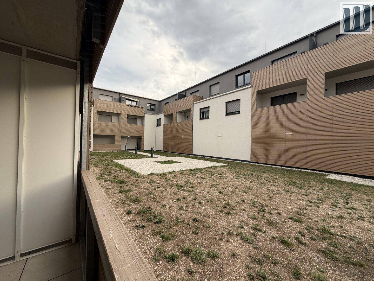 Aussicht vom Balkon auf einen Innenhof mit moderner Architektur und einer zentralen Grünfläche.