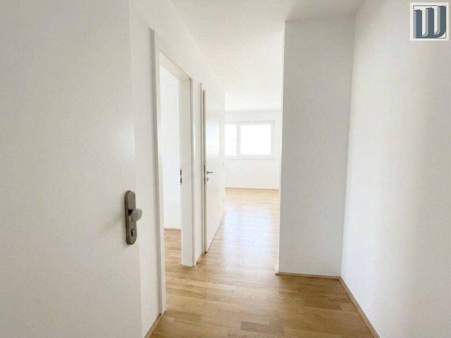 Heller Flur mit Holzboden und weißen Wänden, der zu weiteren Zimmern führt.