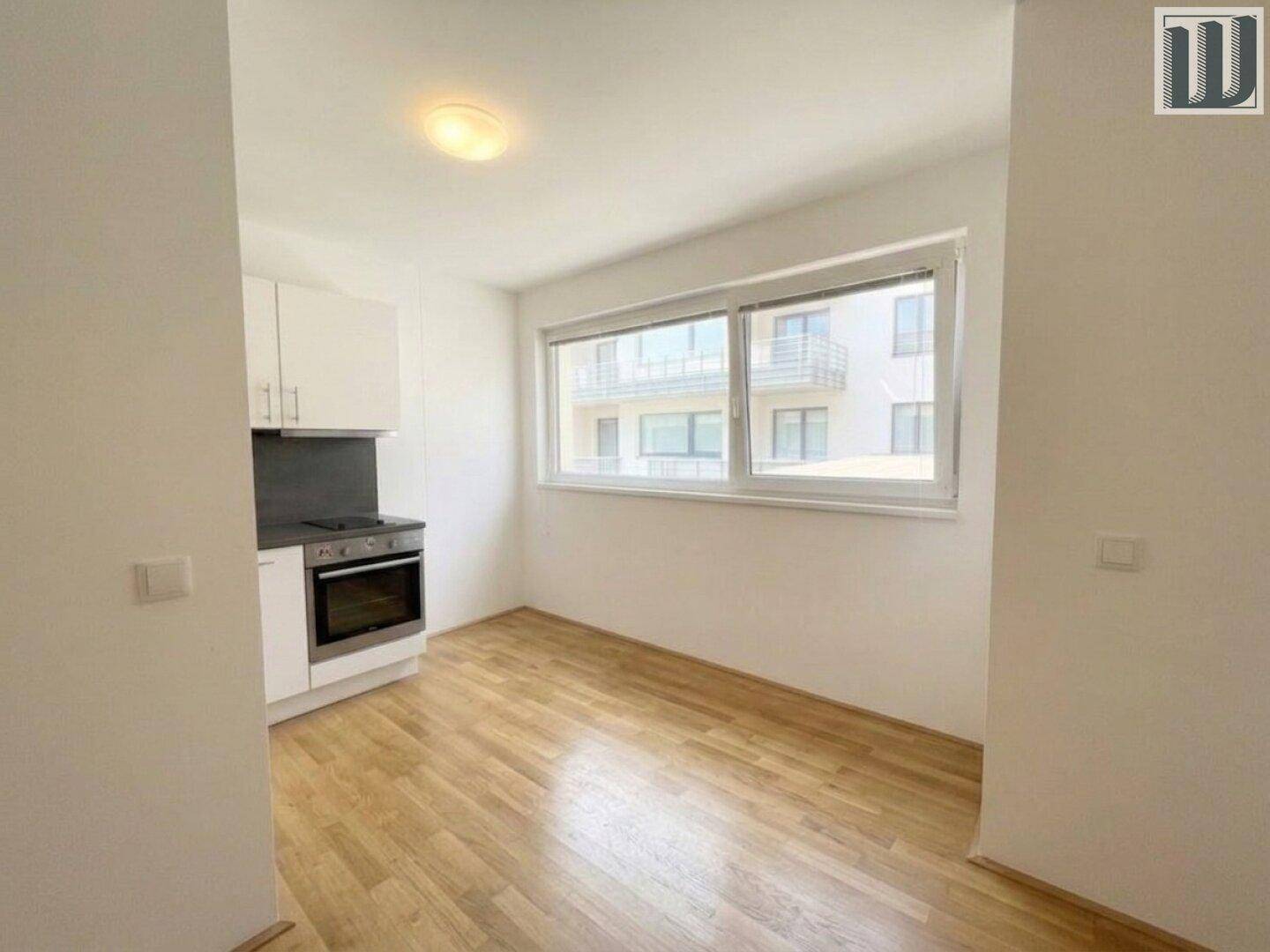 Offene Küchenzeile mit weißen Schränken, integriertem Backofen und Blick nach draußen.