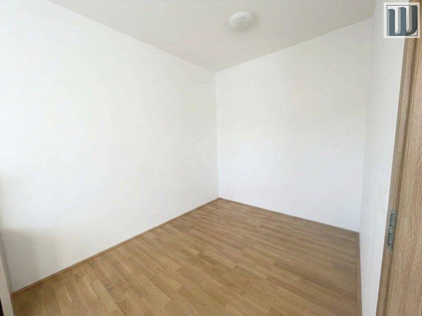 Ruhiges Schlafzimmer mit hellem Holzboden und weißen Wänden, bereit zur individuellen Gestaltung.