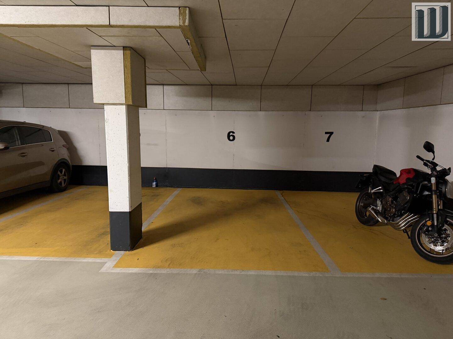 Innenansicht einer Tiefgarage mit markierten Stellplätzen, einem Auto und einem Motorrad.