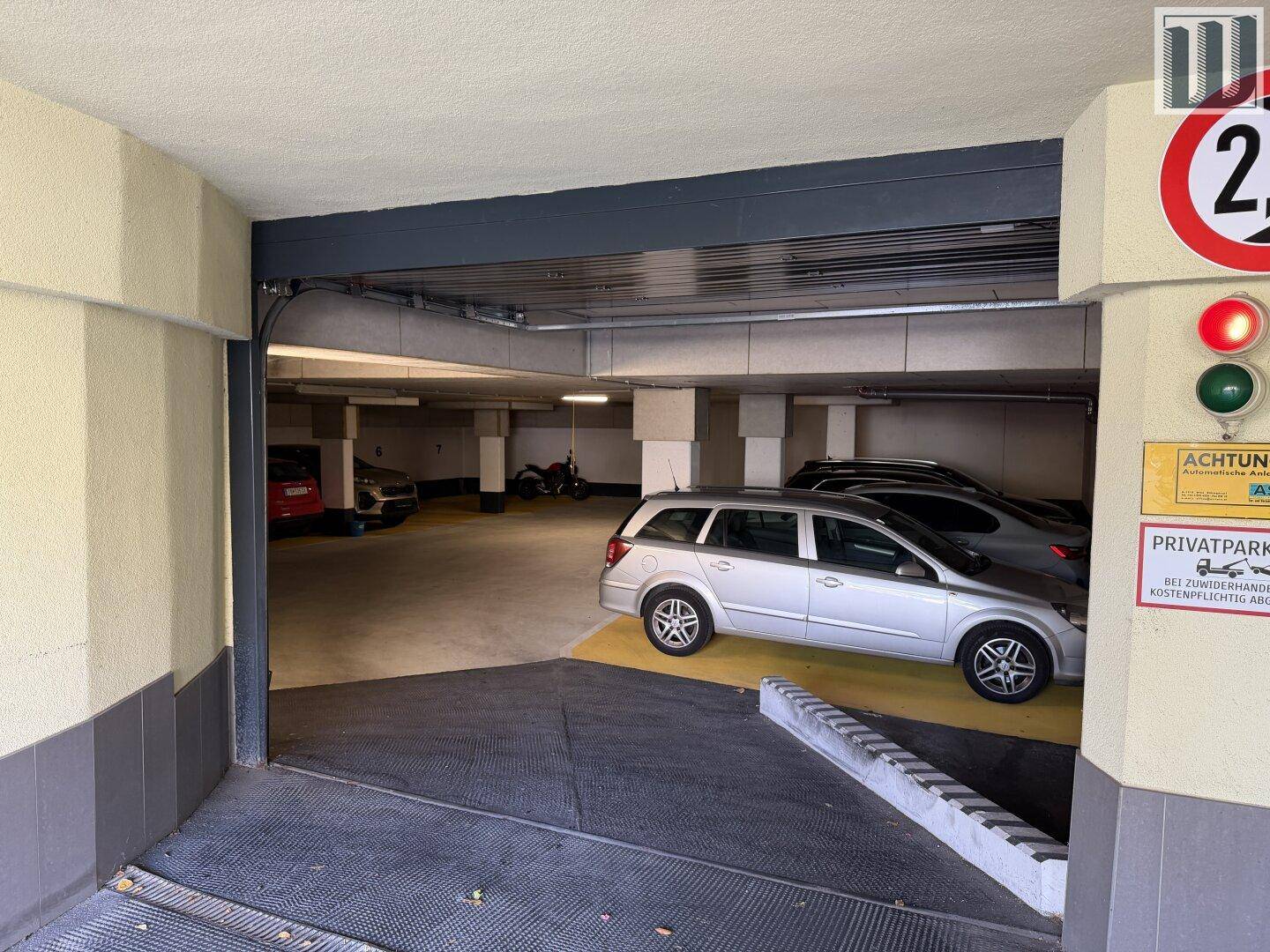 Einfahrt zur Tiefgarage mit Rampe und Blick auf die geparkten Fahrzeuge im Inneren.