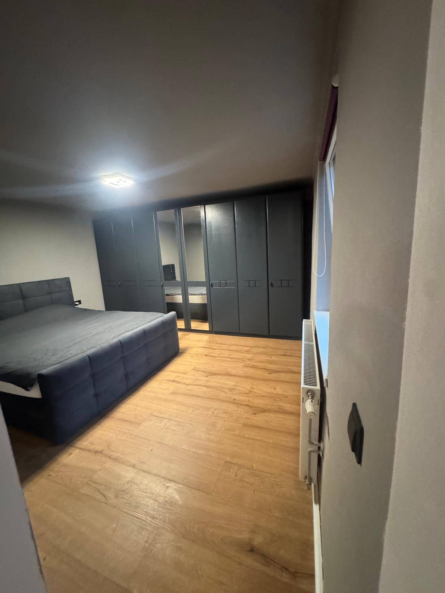 Schlafzimmer mit dunklem Bett, großem Kleiderschrank und hellem Holzfußboden.