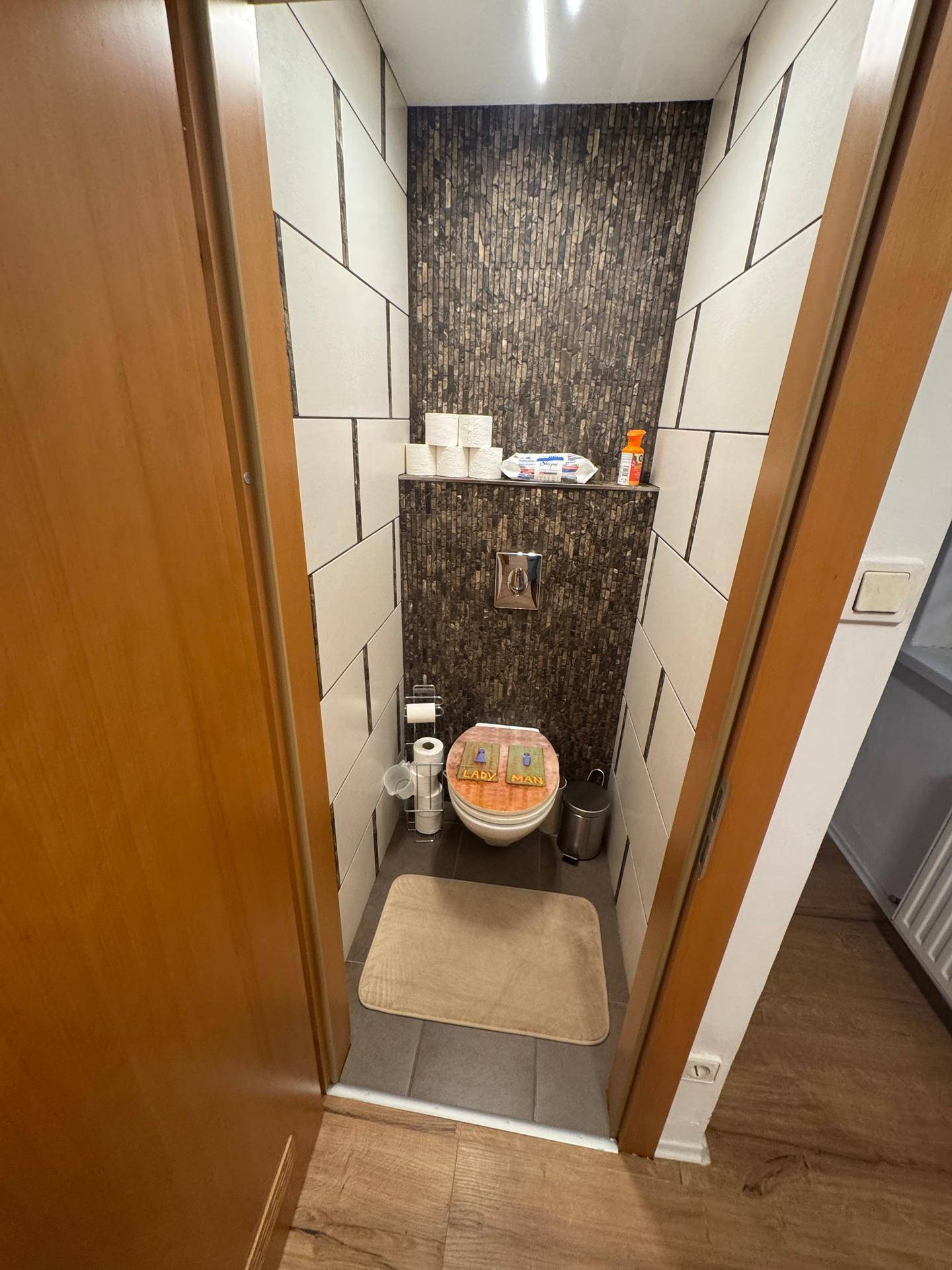 Kleines WC mit modernen Fliesen an den Wänden und dunklem Mosaikakzent.