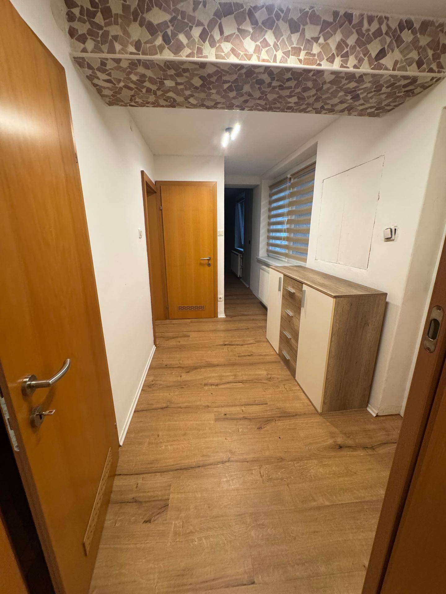 Flur mit hellem Holzfußboden, Holzmöbeln und einer strukturierten Decke.