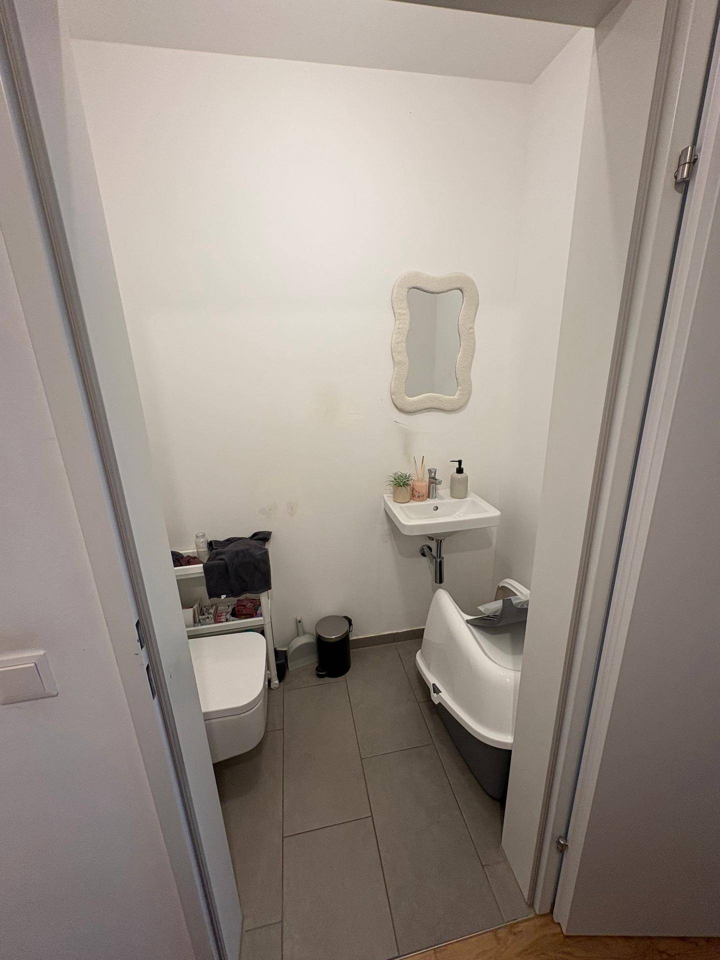 Kleines Gäste-WC mit Toilette, Waschbecken und Fliesenboden in schlichtem Design.