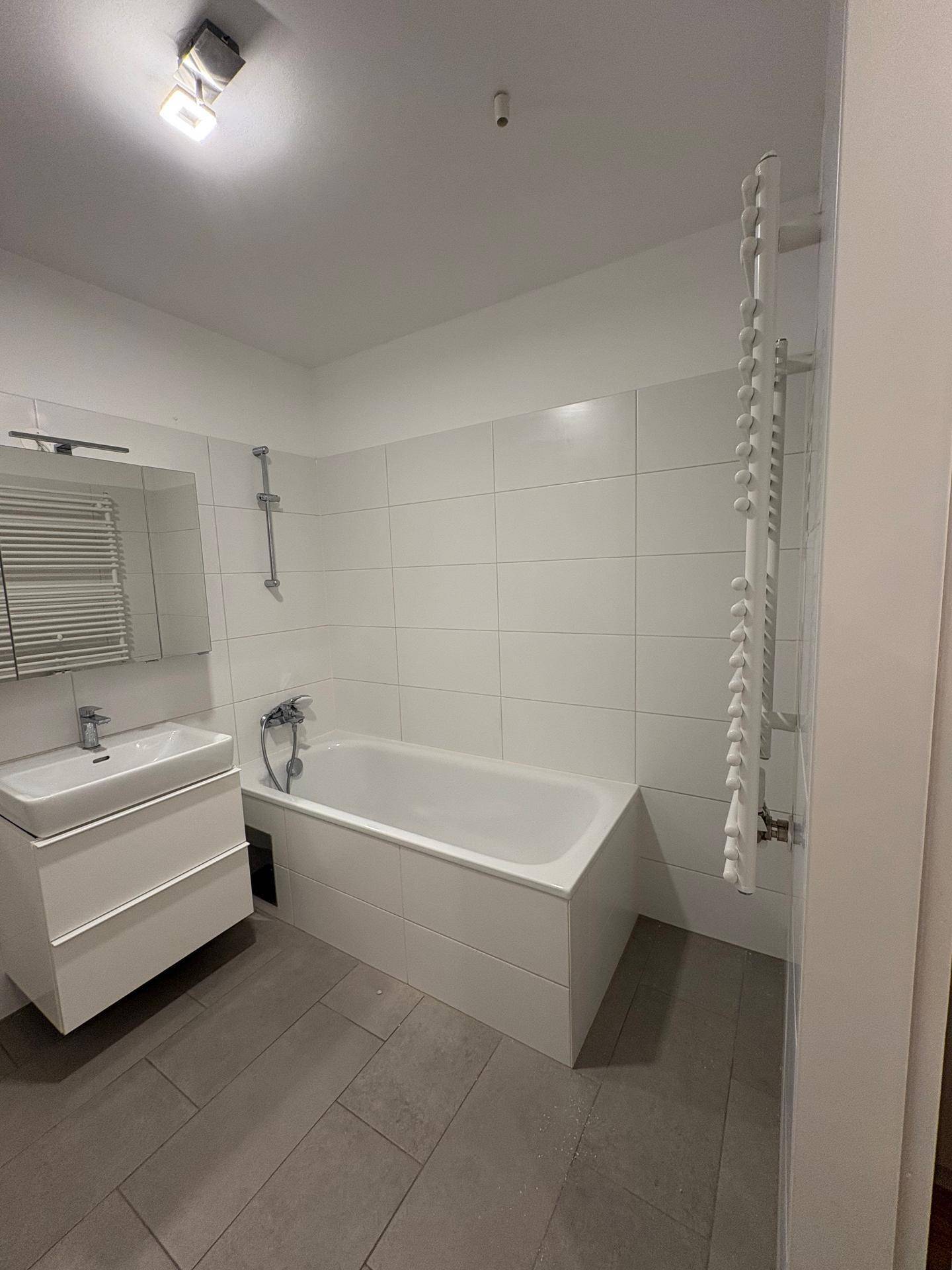 Modernes Badezimmer mit Badewanne, Waschtisch, Spiegel und beheiztem Handtuchhalter.