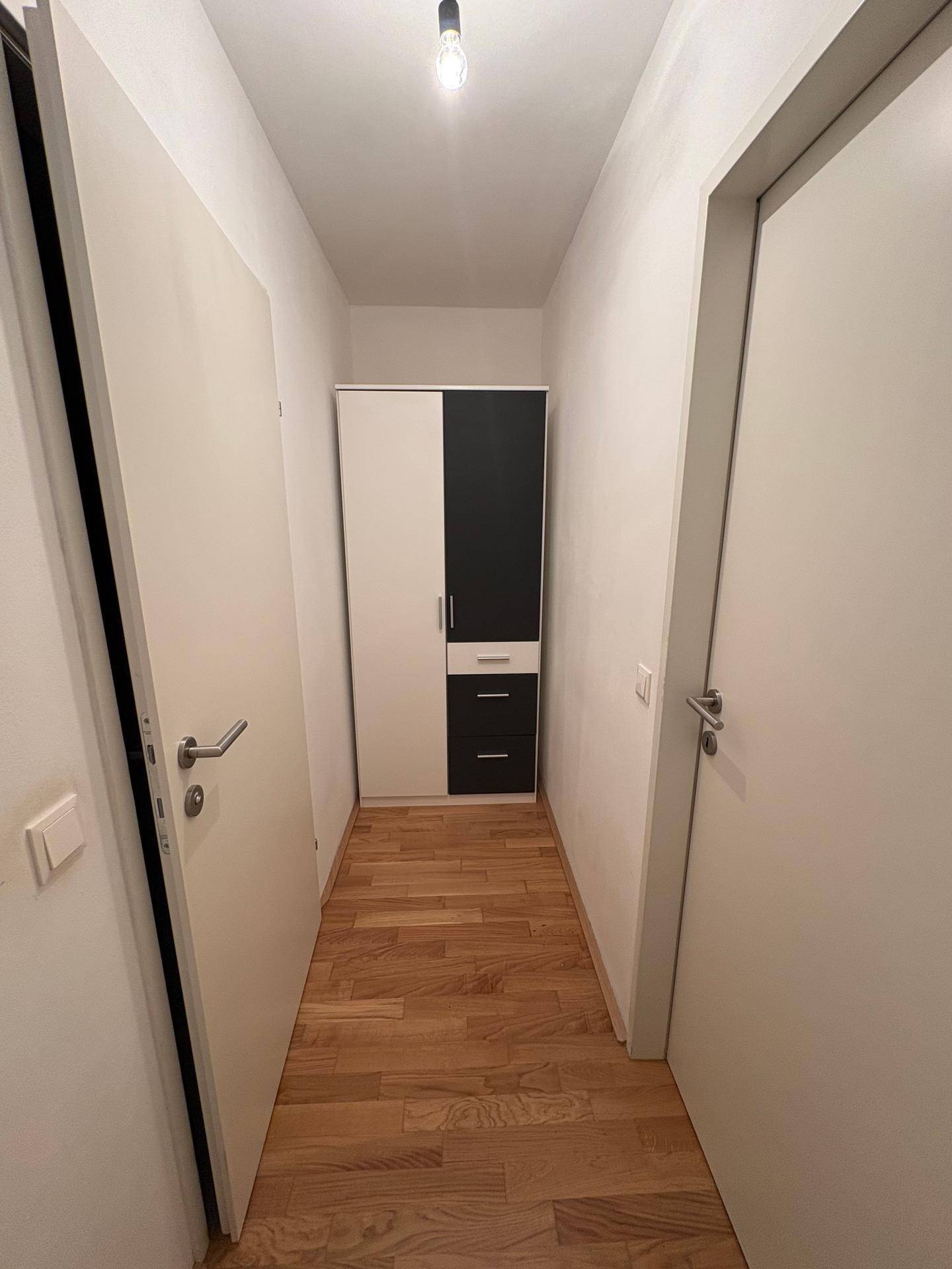 Schmaler Flur mit praktischem zweifarbigem Kleiderschrank und hellem Holzfußboden.